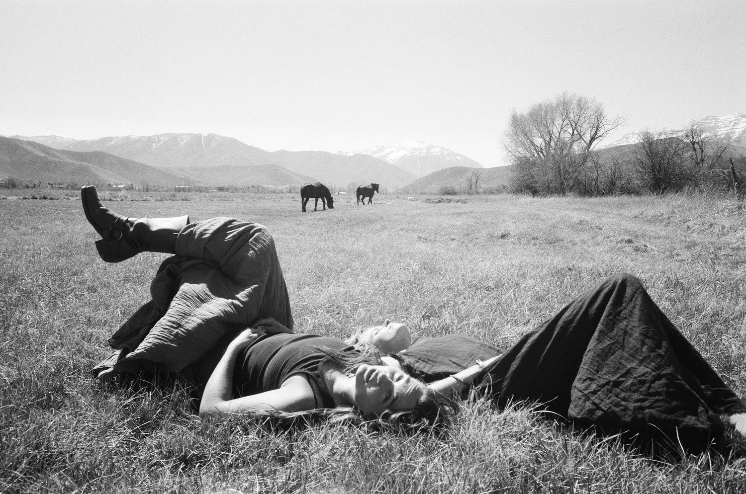 Black and white 35mm film portrait of two women lying in a field with horses in the Utah landscape.
