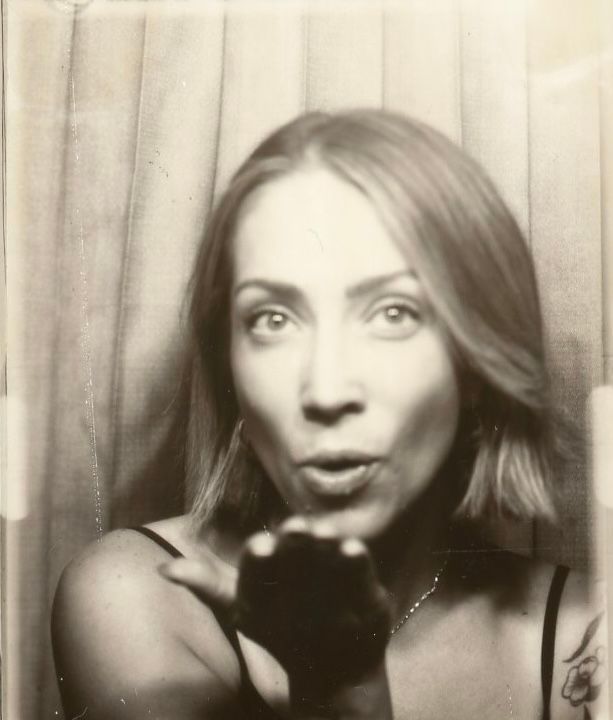 Black and white photo booth portrait of a woman blowing a kiss toward the camera.