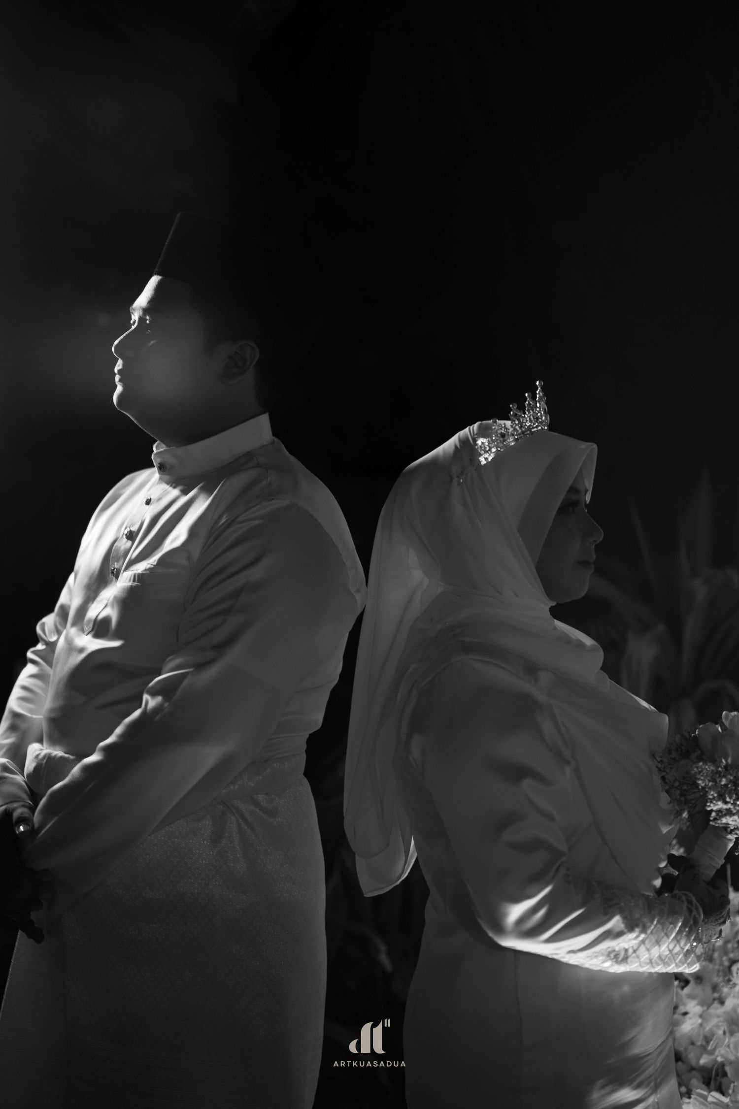 Black and white photo of a Muslim couple in traditional attire standing back to back at their wedding ceremony.