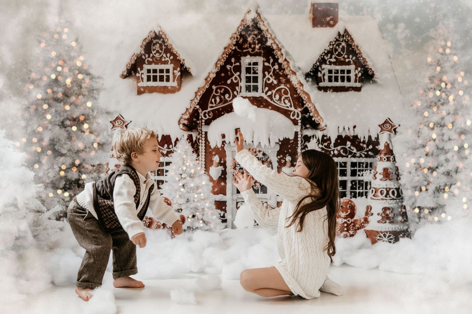 Christmas mini sessions with kids tossing snow, laughing, and making magical holiday memories during a festive gingerbread house photography
