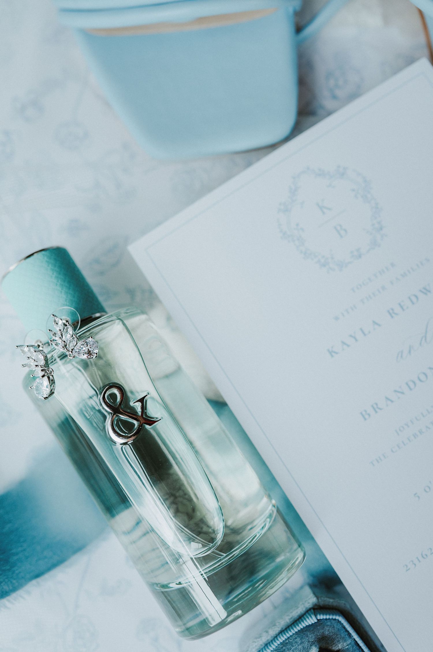 Wedding detail shot earrings , perfume and invitation.