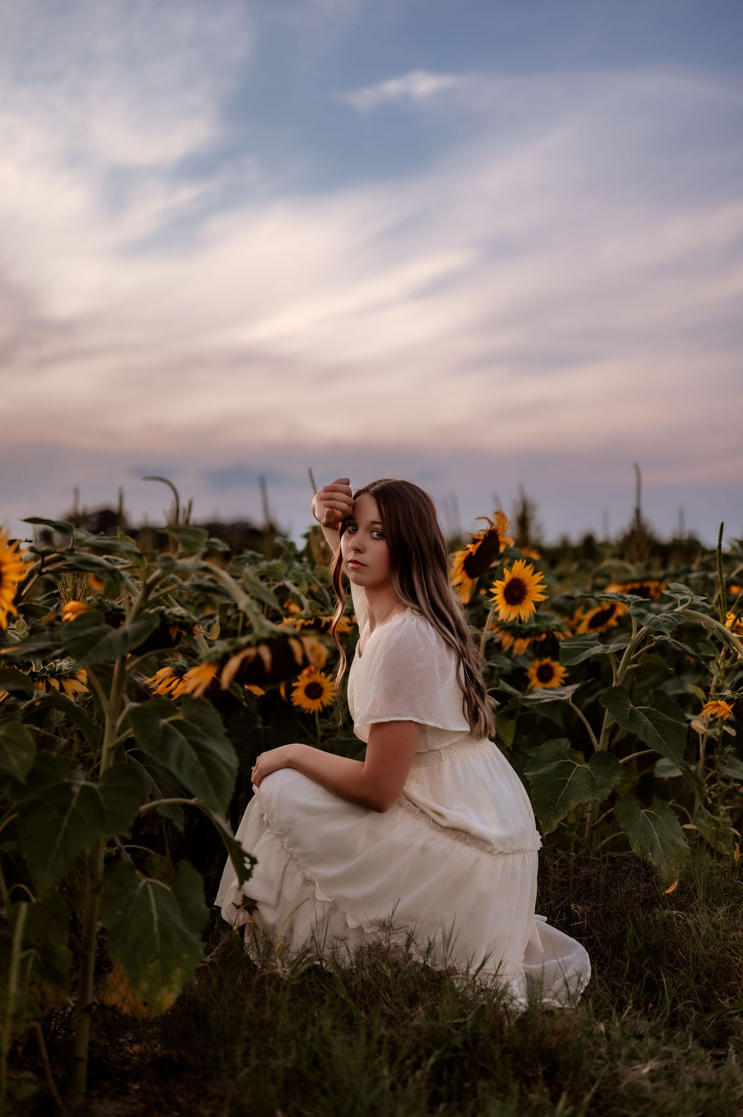 Senior girl photo session in a sunflower field beneath a vibrant cotton candy sky with colorful, dreamy, slightly moody tones.