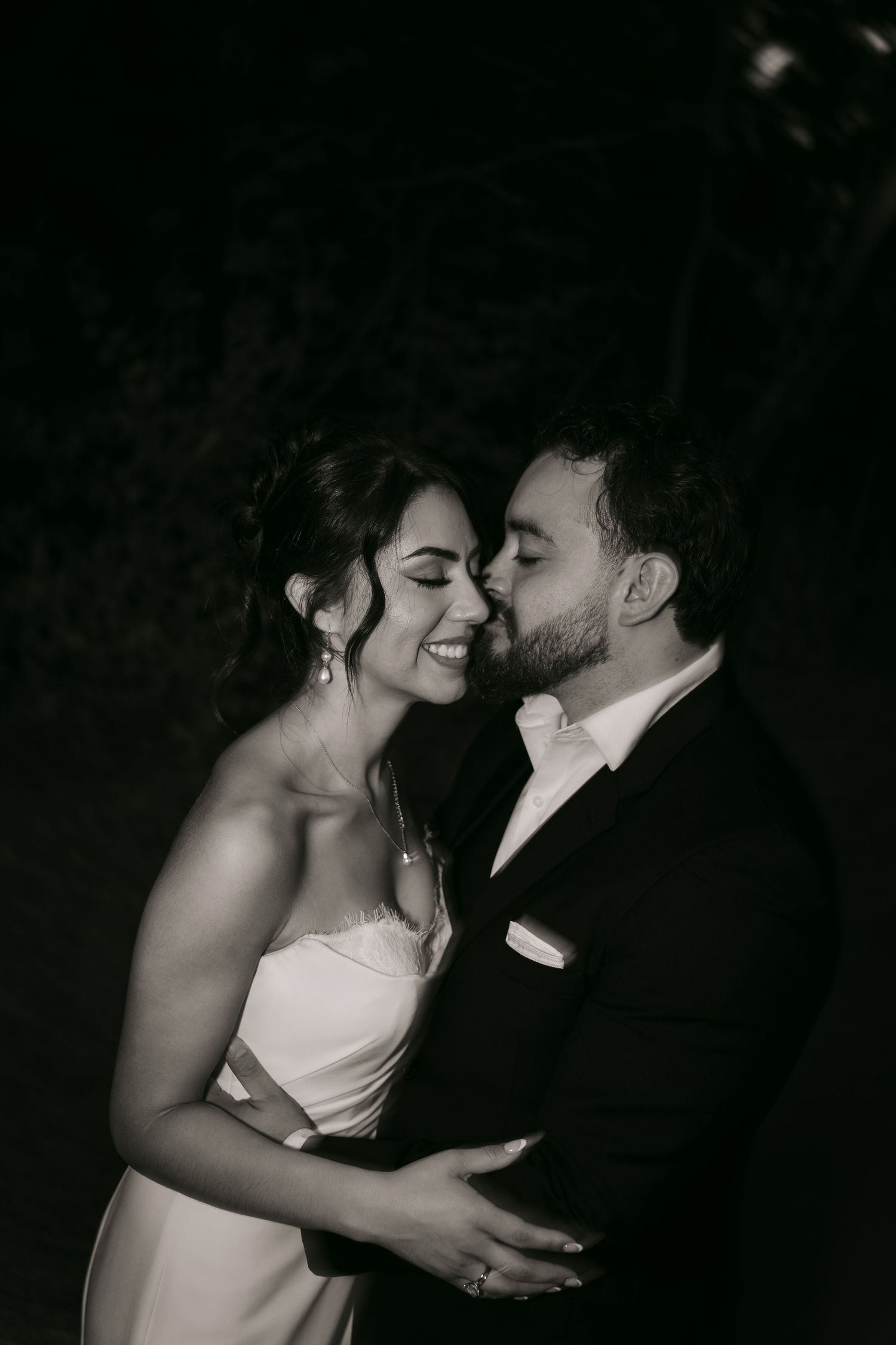 Black and white portrait of smiling bride and groom embracing intimately outdoors at night.