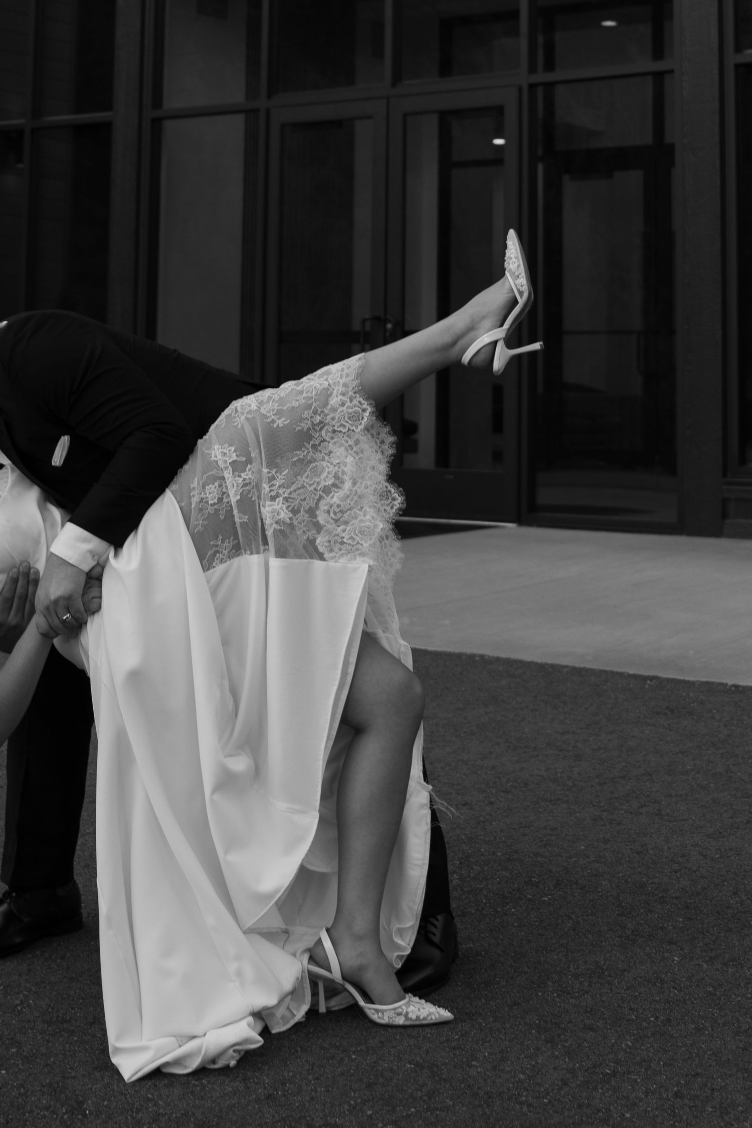 Black and white close-up of groom dipping bride, showcasing her lace wedding dress and heels.
