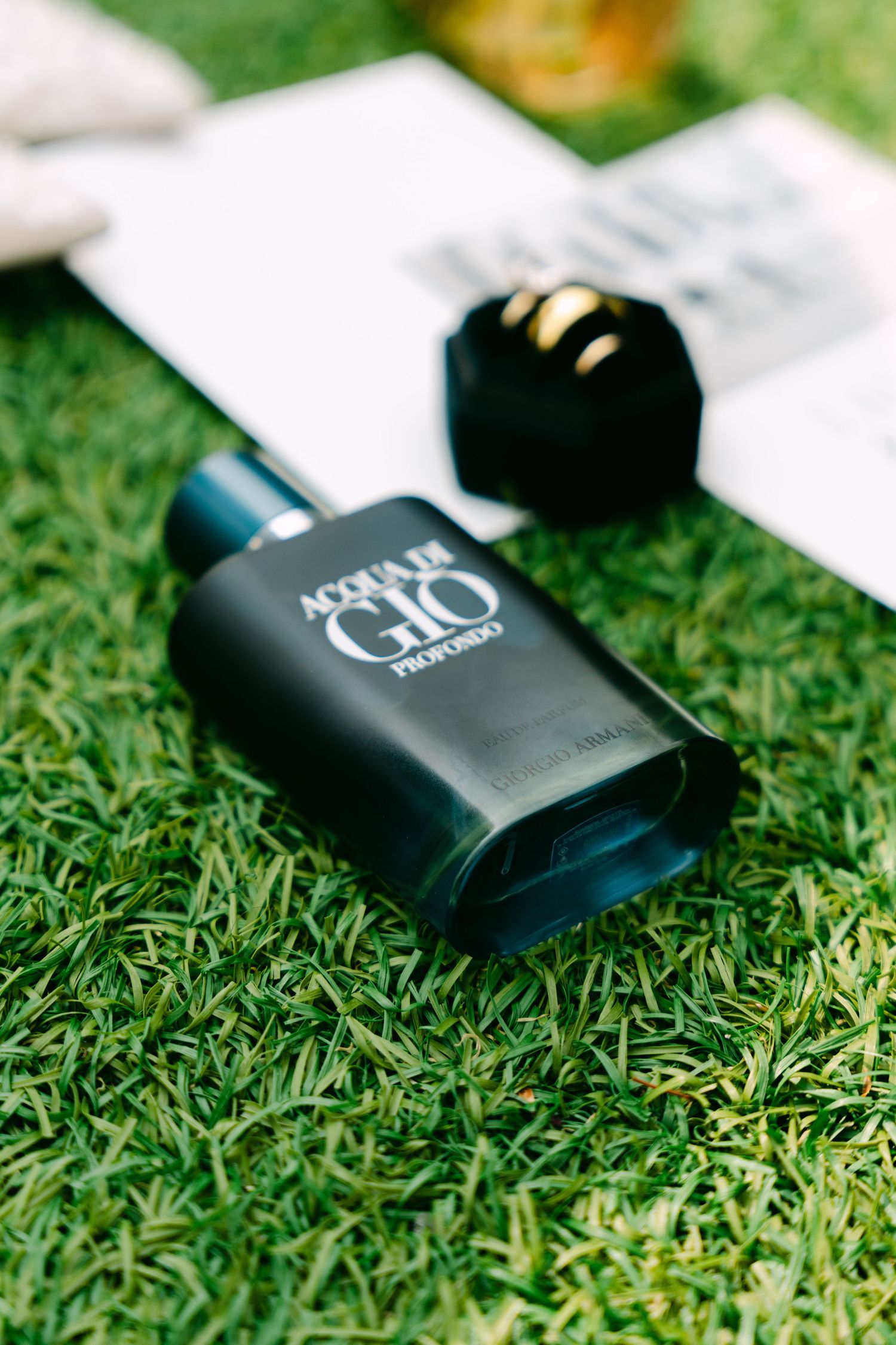 Acqua di Gio Profondo cologne bottle lying on green grass next to a black velvet ring box.