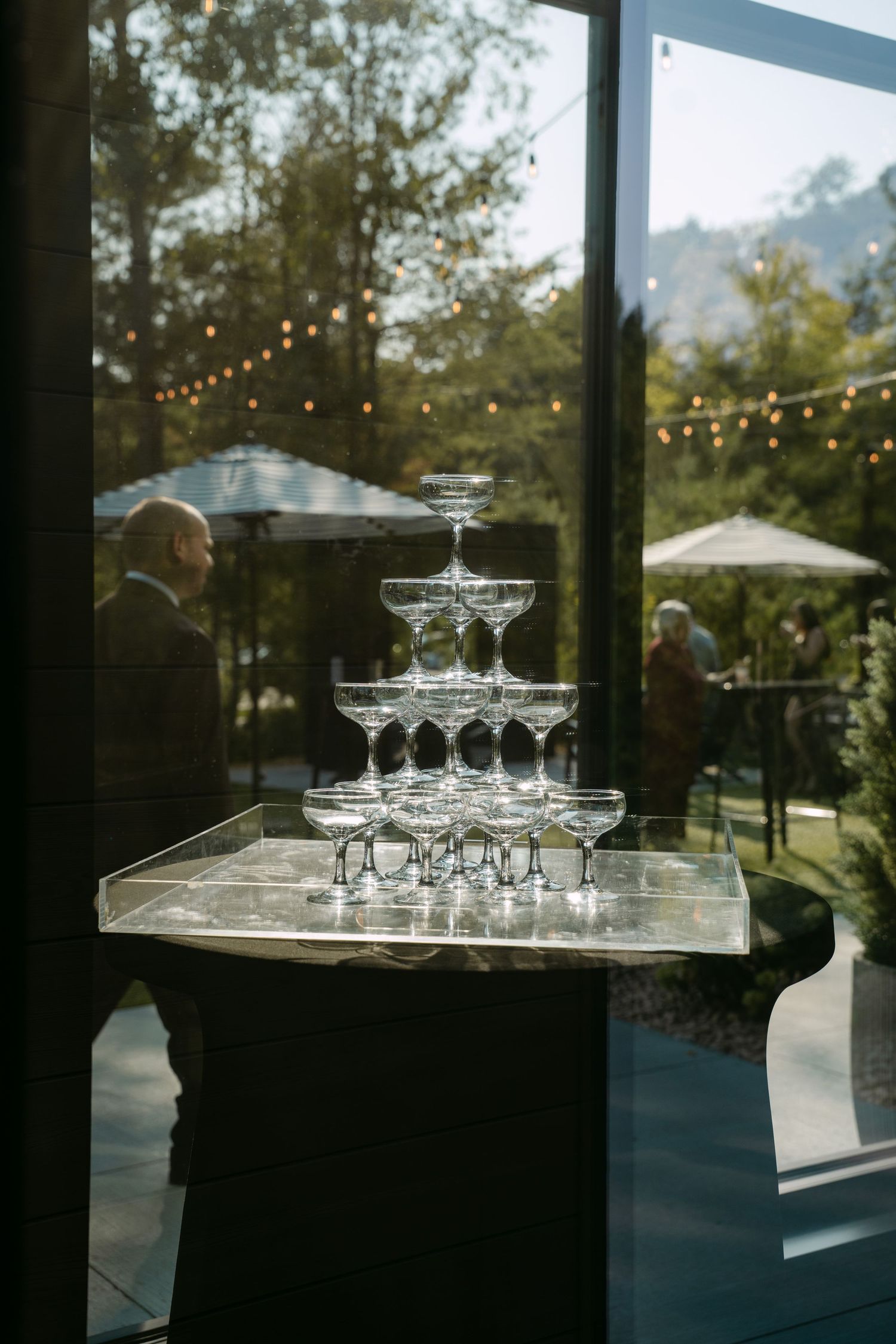 Elegant champagne tower of coupe glasses displayed on marble tray near large venue window.