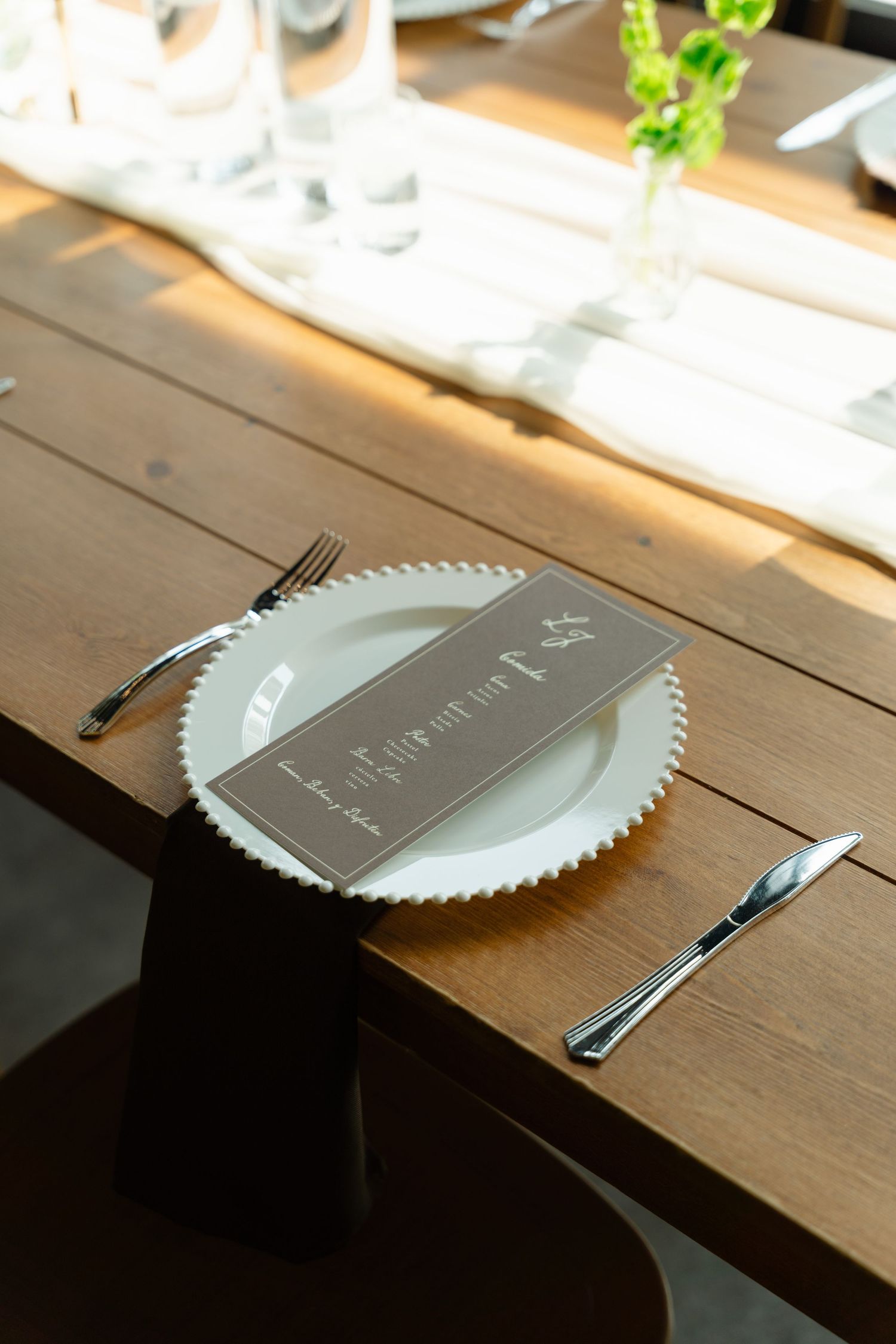 Close-up of wedding place setting with charger plate, brown menu card, and silverware.