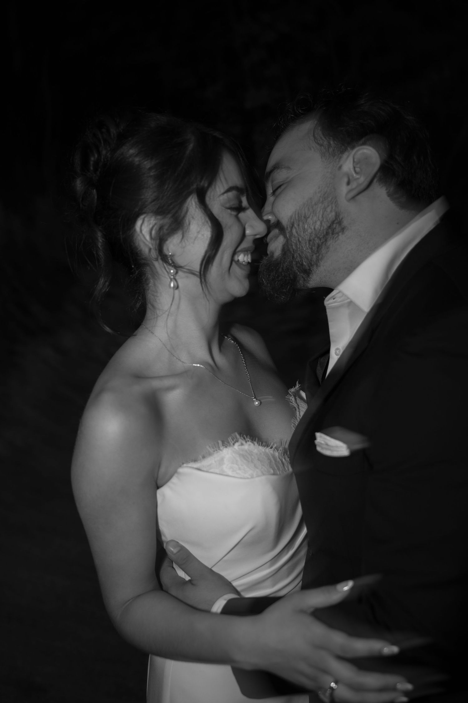 Black and white photo of laughing bride and groom sharing a joyful romantic moment at night.