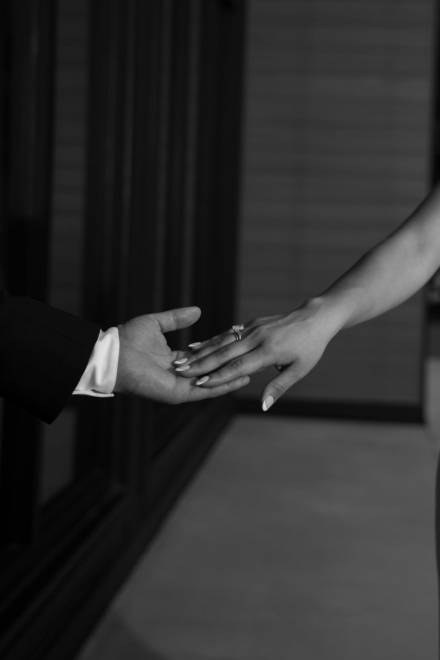 Black and white close-up of bride and grooms hands reaching toward each other, showing wedding ring.