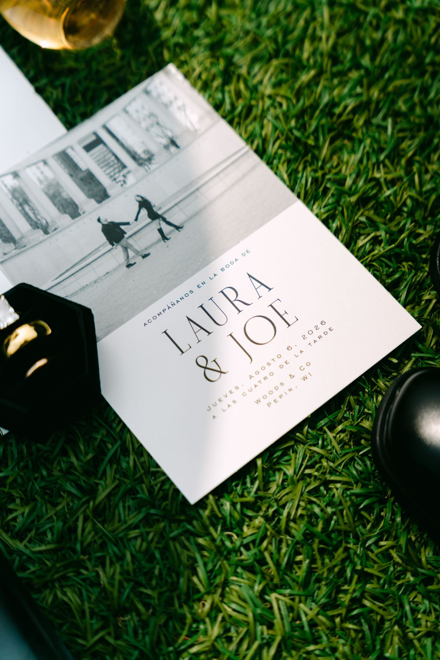 Close-up of Laura and Joe wedding invitation with black and white engagement photo on green grass.