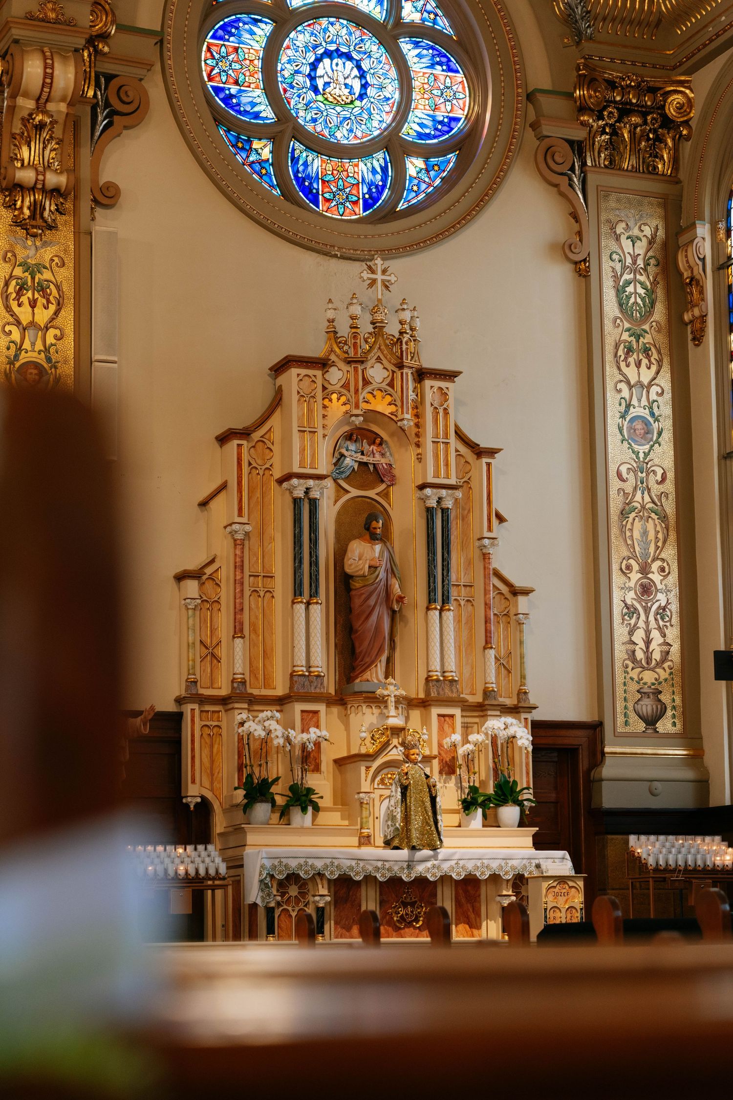 Ornate church altar with golden details, religious statue, and colorful stained glass rose window.