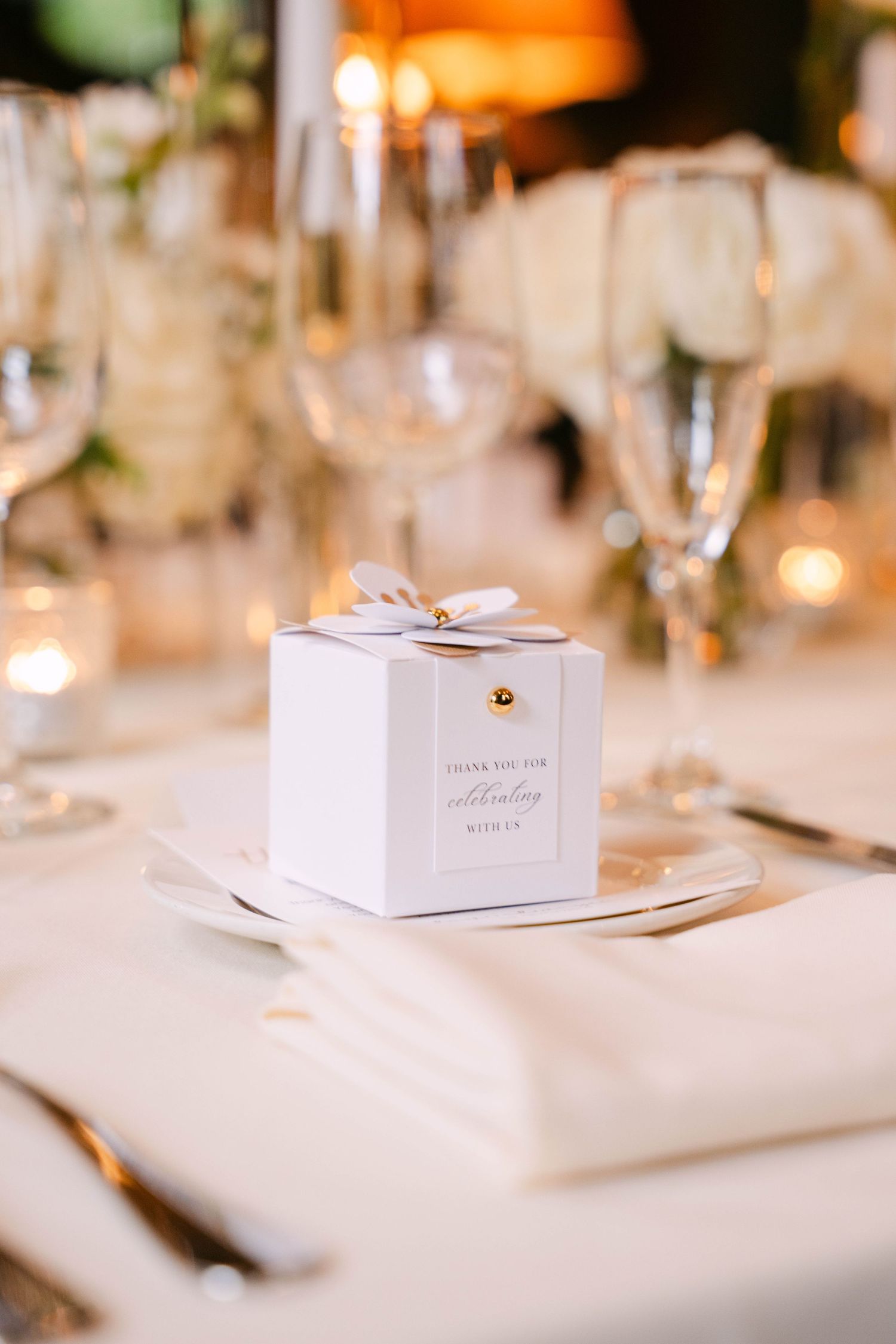 Elegant white wedding favor box with ribbon on reception dinner table setting.