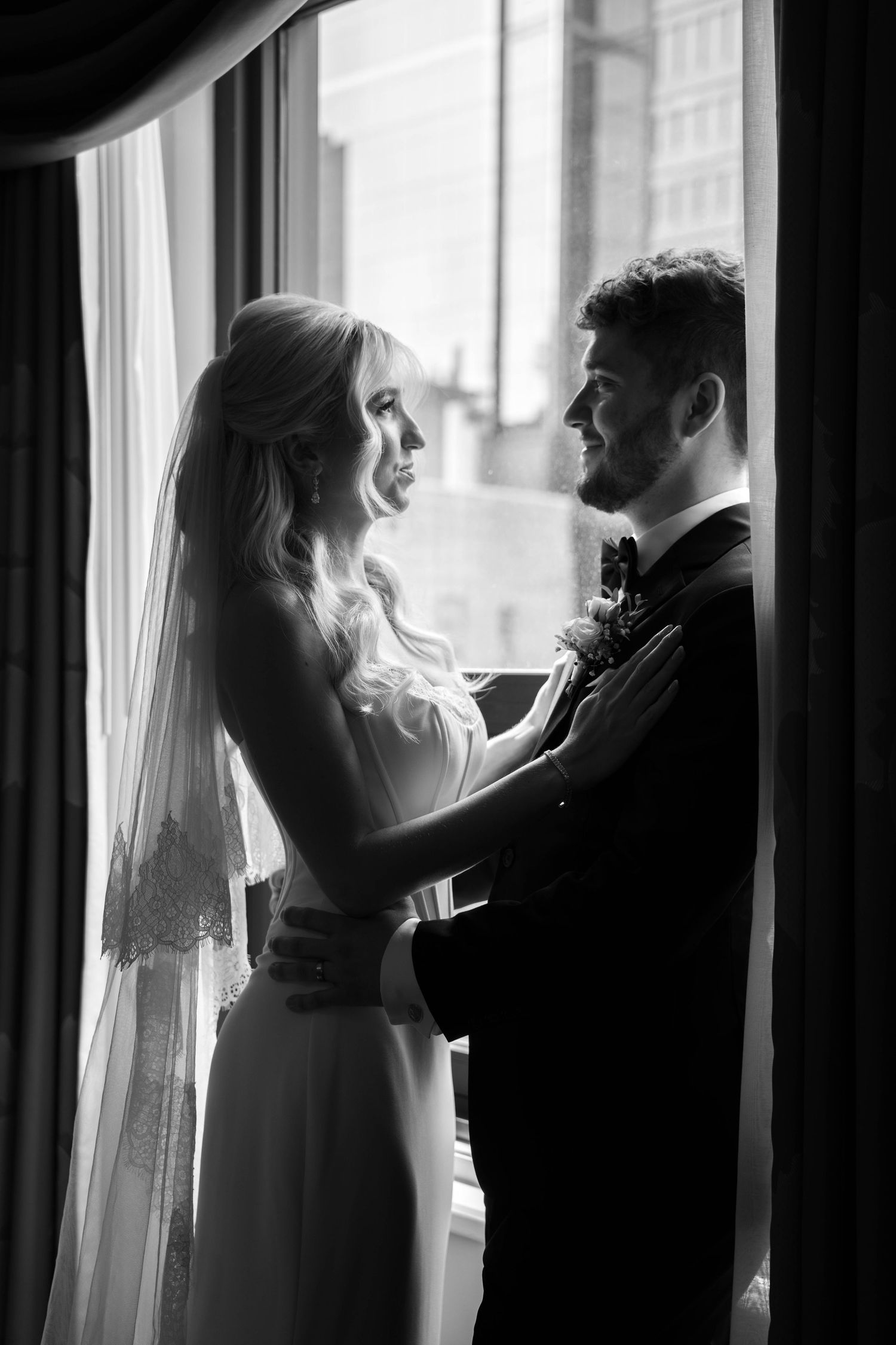 Bride and groom share a romantic moment by a window in a stunning black and white wedding portrait.