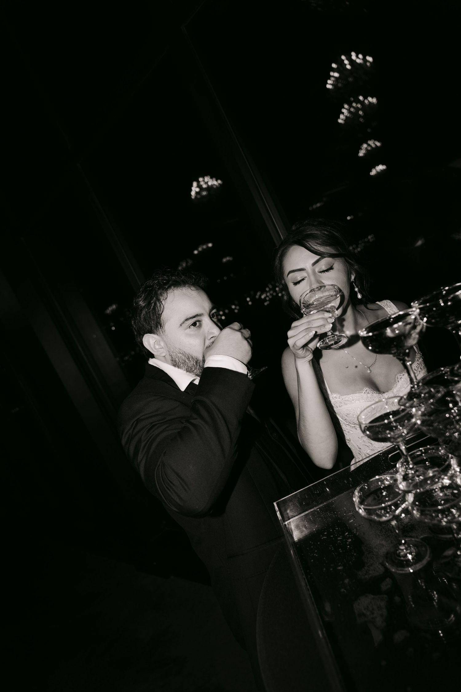Black and white photo of bride and groom drinking champagne together at wedding reception.