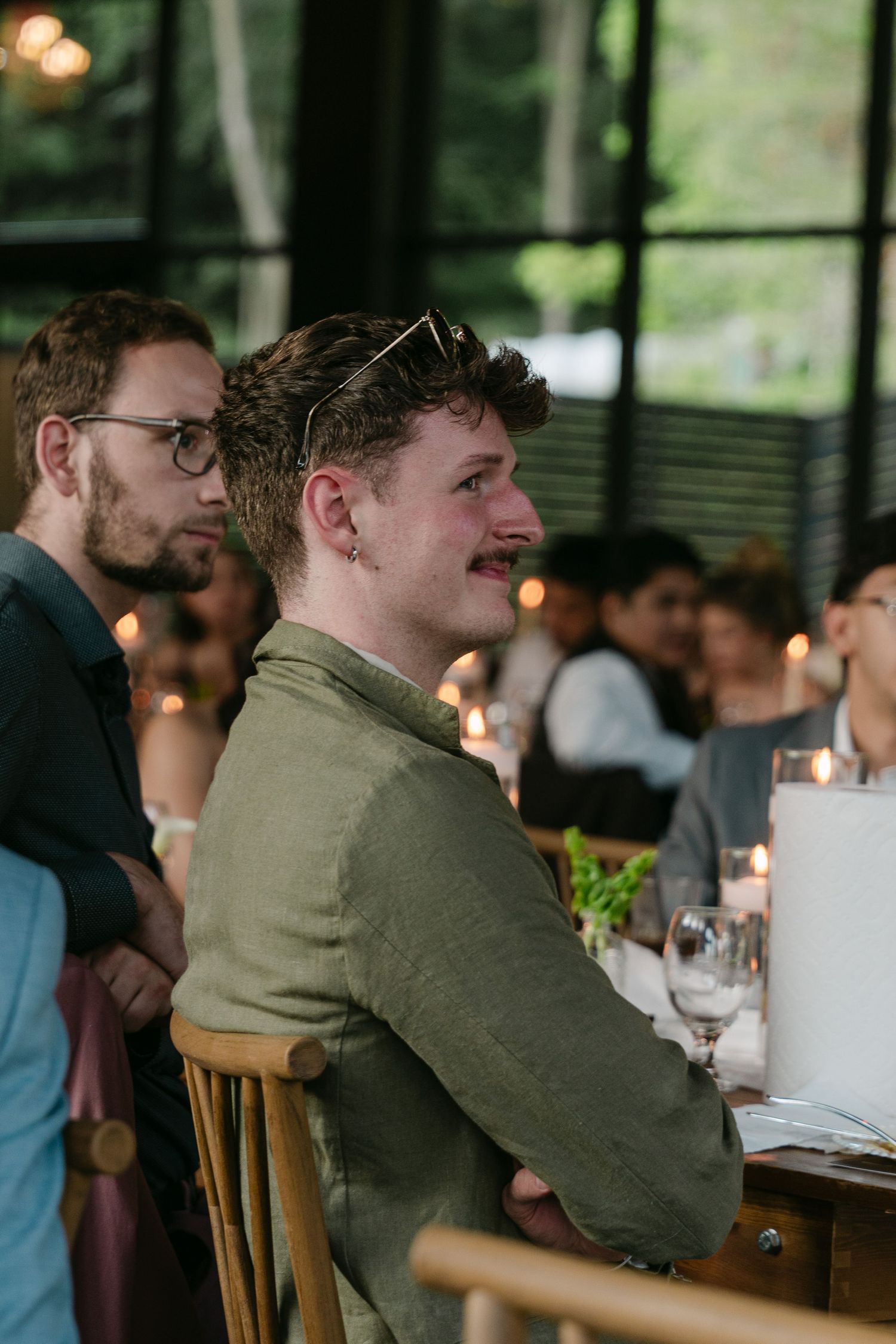 A wedding guest in a green linen shirt smiles warmly during a candlelit reception dinner.