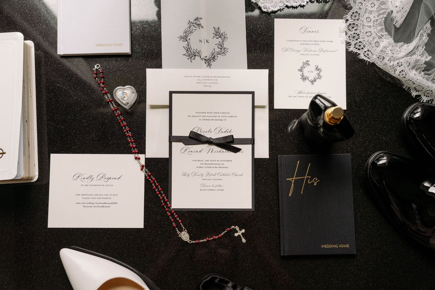 Elegant black and white wedding invitation suite with ribbon, rosary beads, and accessories on dark background.