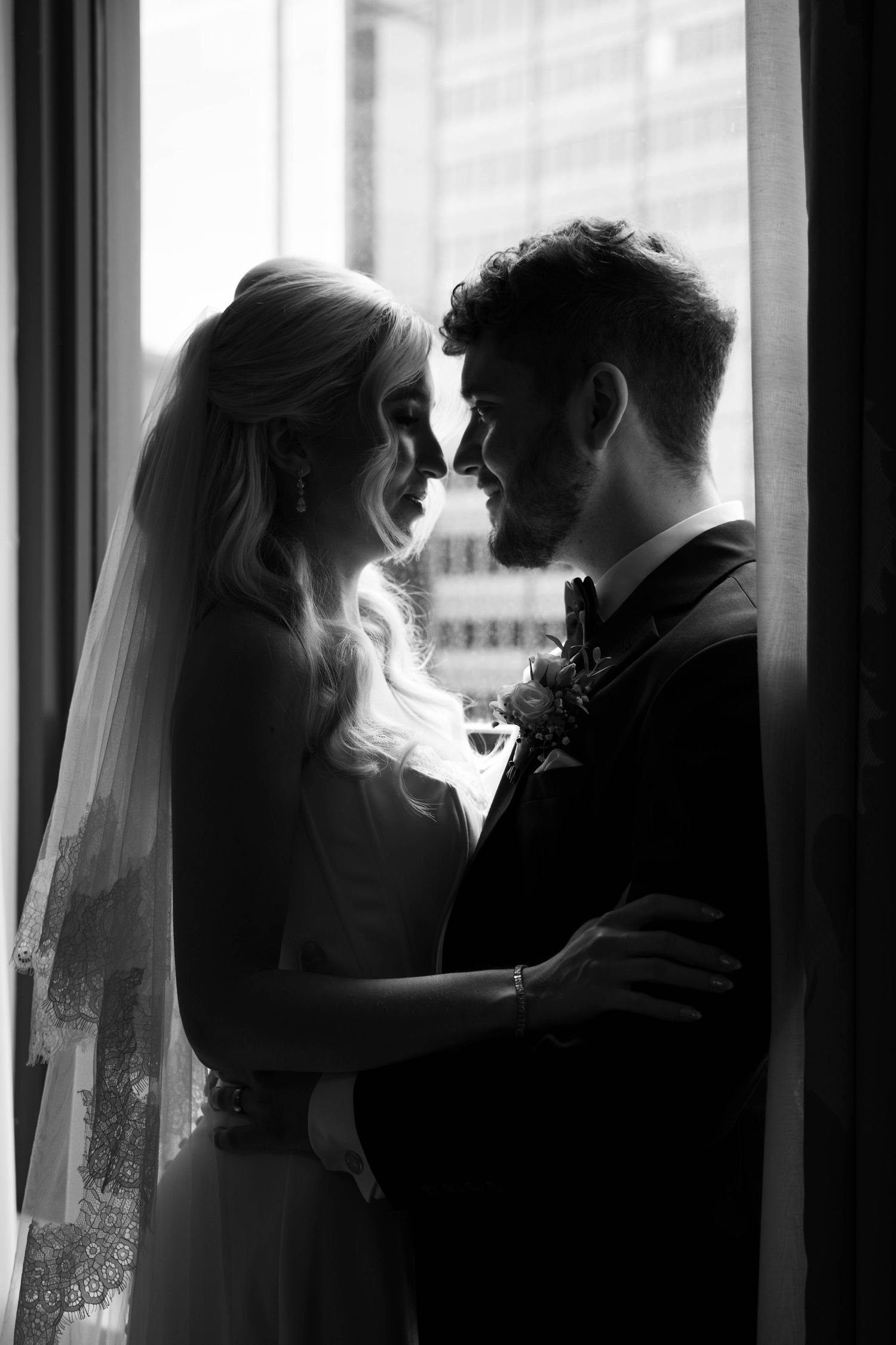 Black and white photo of bride and groom sharing an intimate moment by a window on their wedding day.