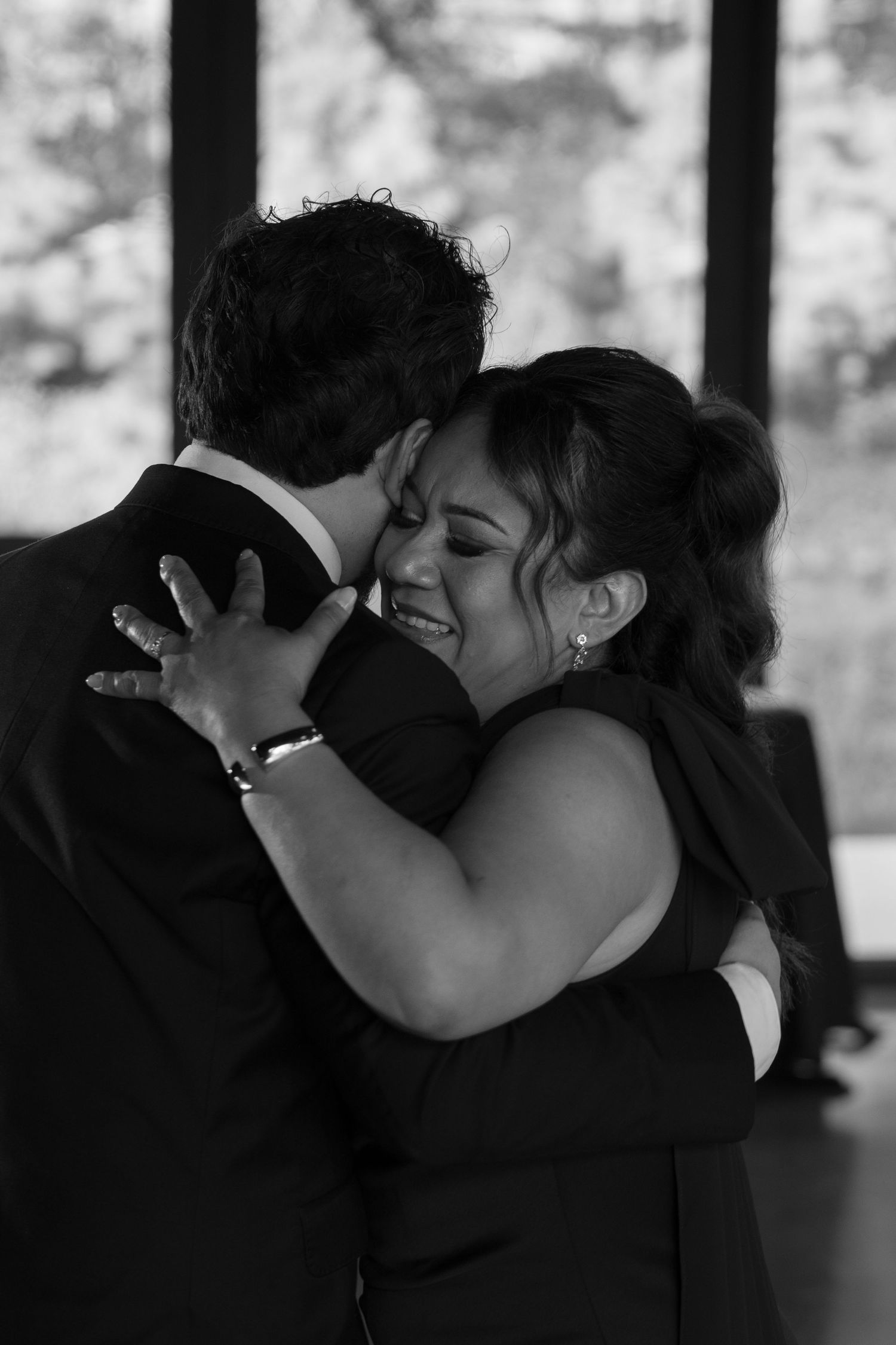 Groom and mother share emotional embrace during mother-son wedding dance in black and white reception photo.