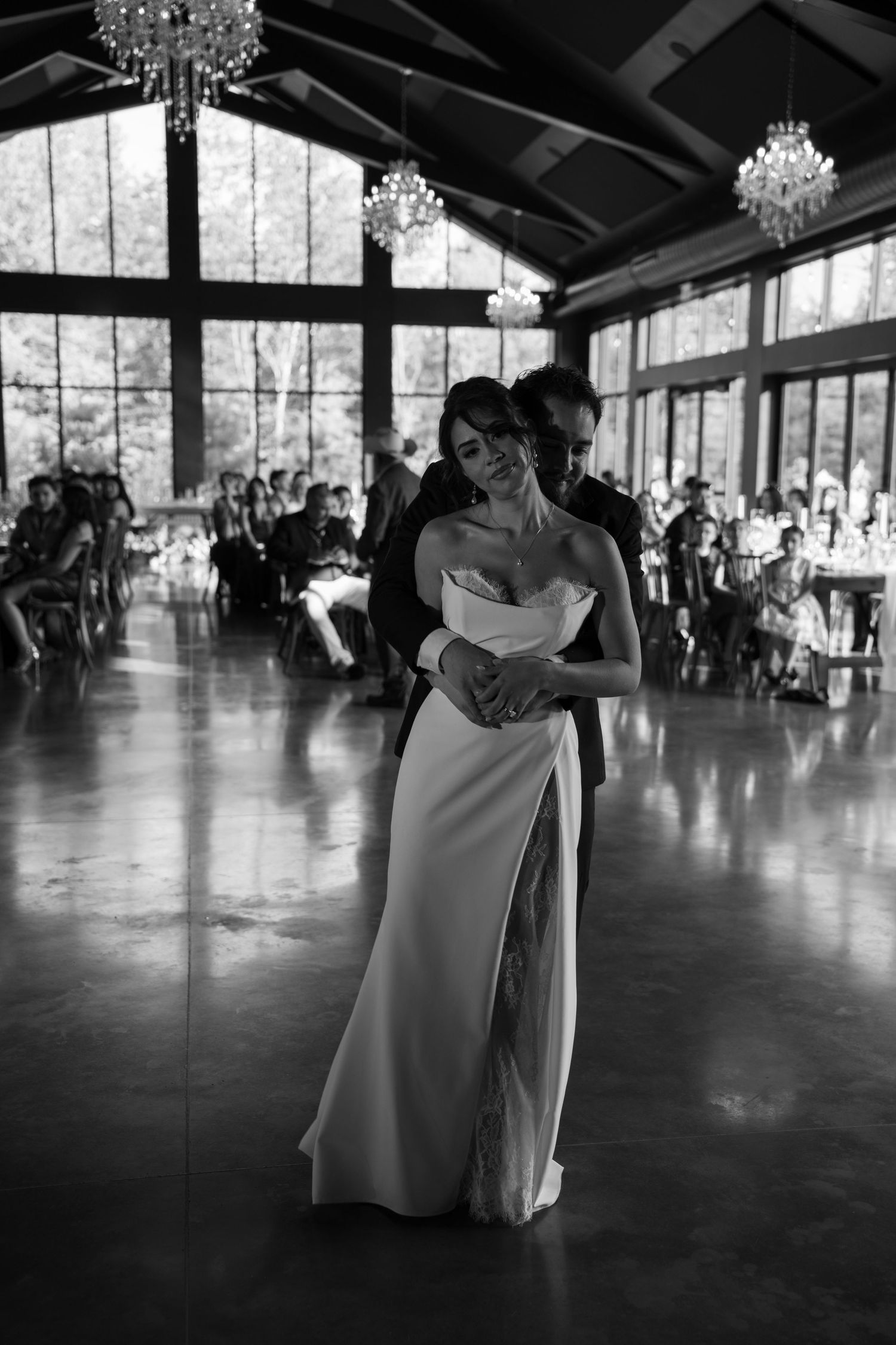 Bride and groom share first dance in stunning black and white photo inside chandelier-lit wedding reception hall.