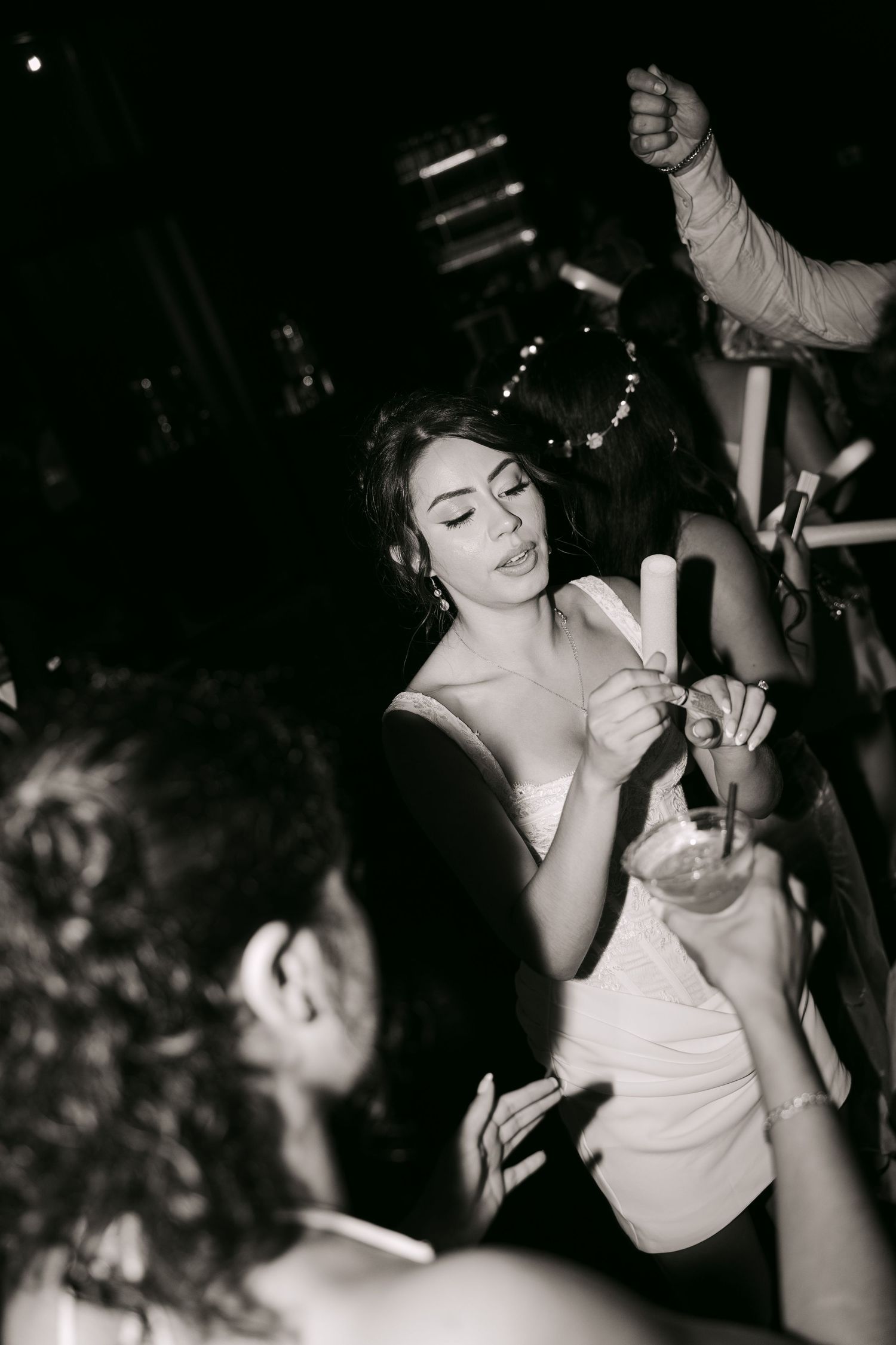 Black and white photo of bride holding sparklers and cocktail while celebrating at wedding reception.