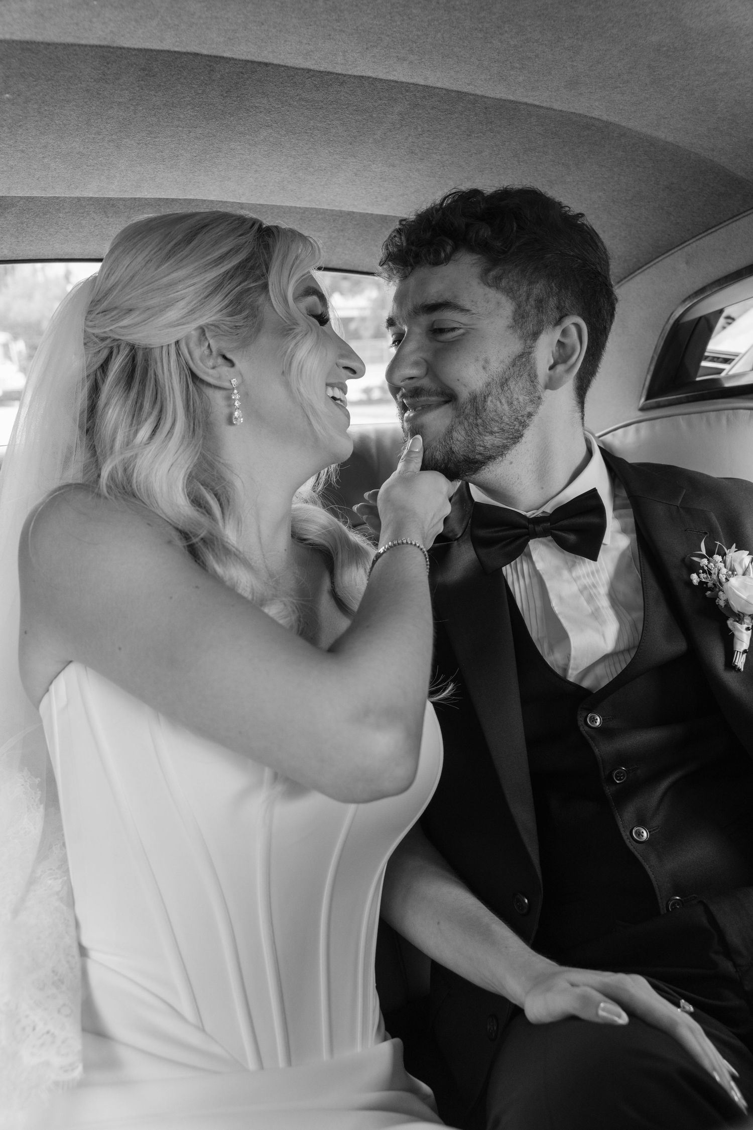 Black and white photo of bride and groom sharing a tender moment in vintage car.