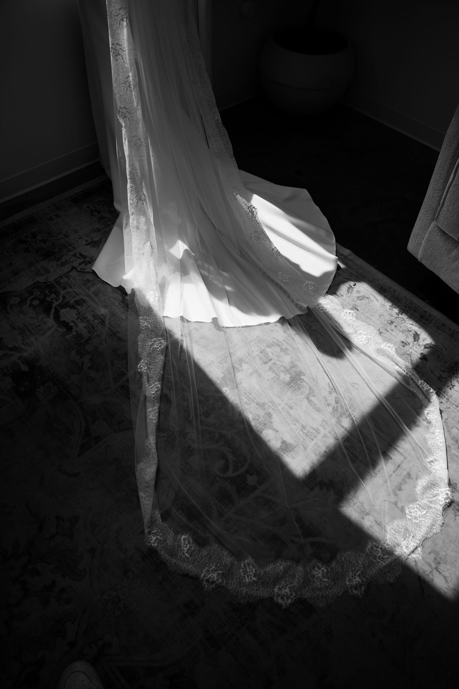 Black and white photo of wedding dress train spread on floor in dramatic light.