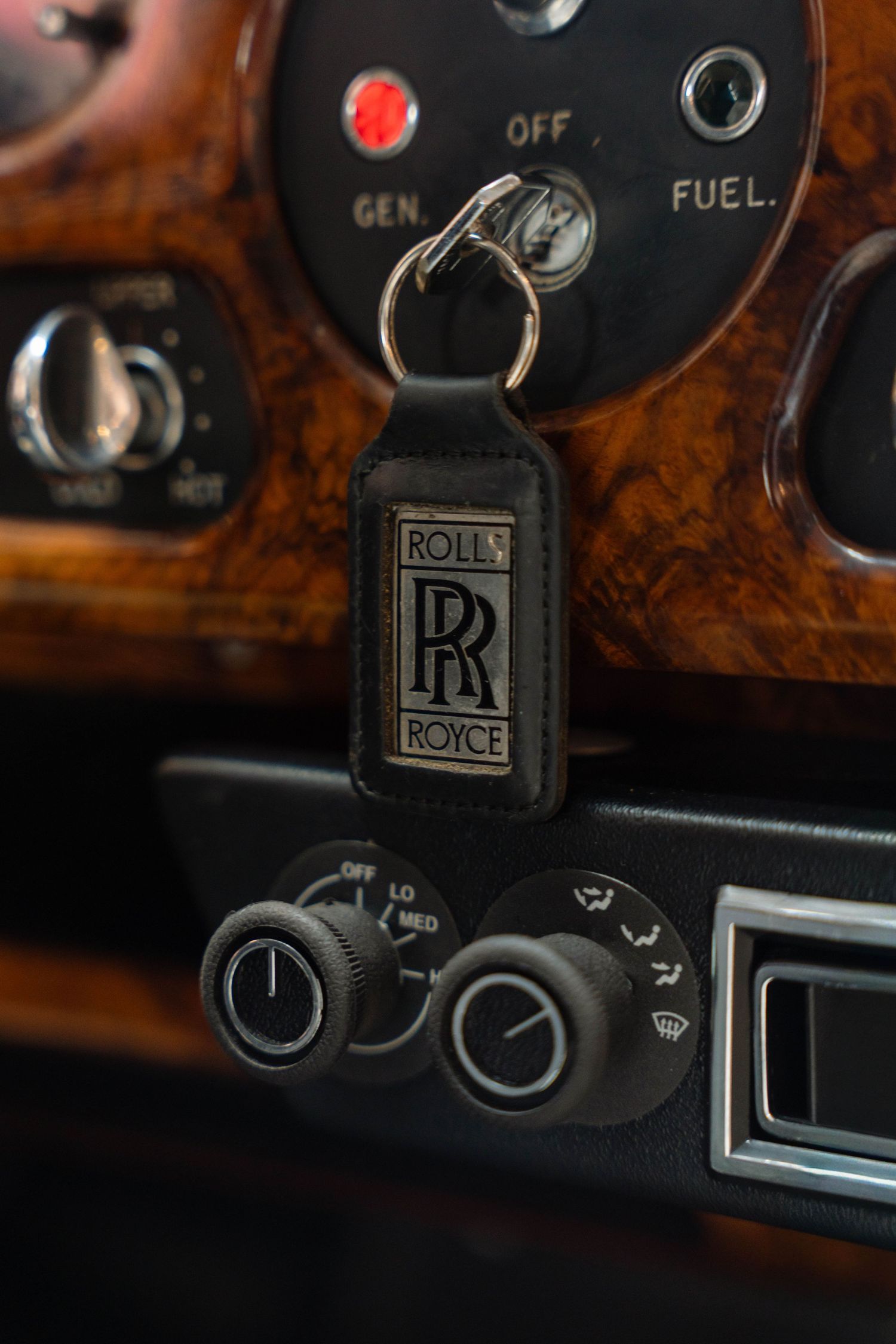 Close-up of a Rolls-Royce leather keychain in the ignition of a classic luxury car dashboard.