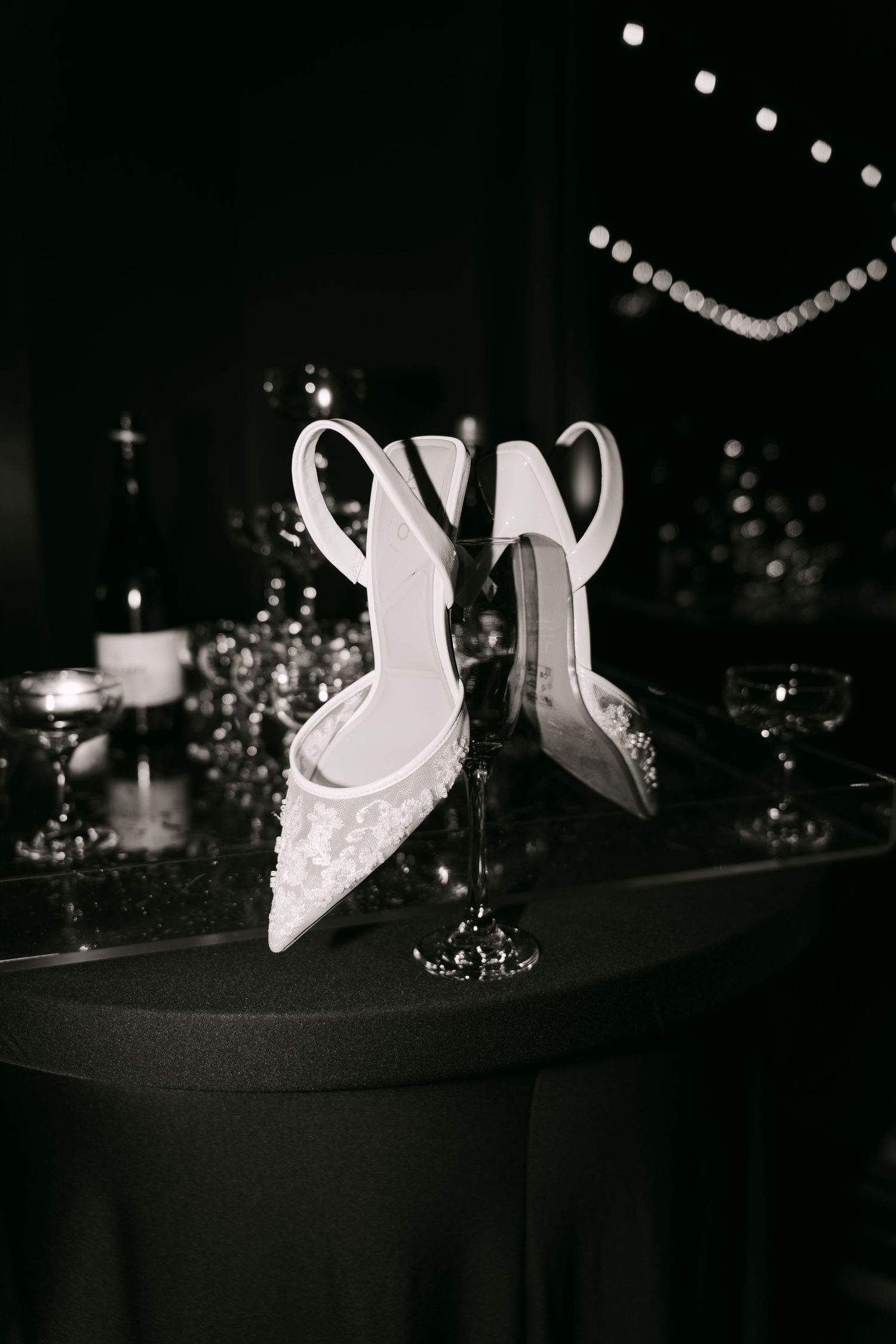 Black and white photo of elegant embellished bridal heels displayed on wedding reception table.