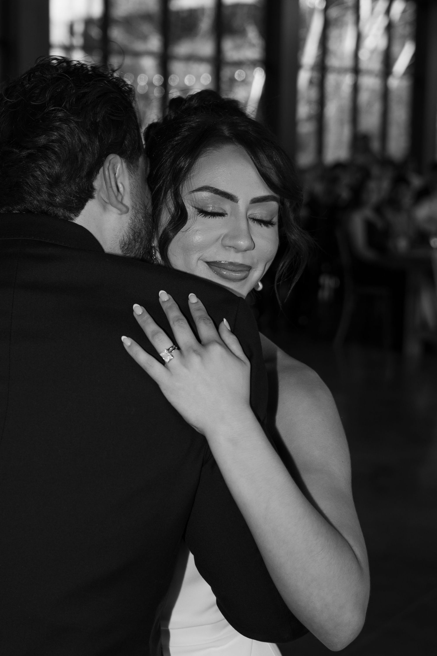 Black and white photo of bride with closed eyes smiling while embracing groom on the dance floor.
