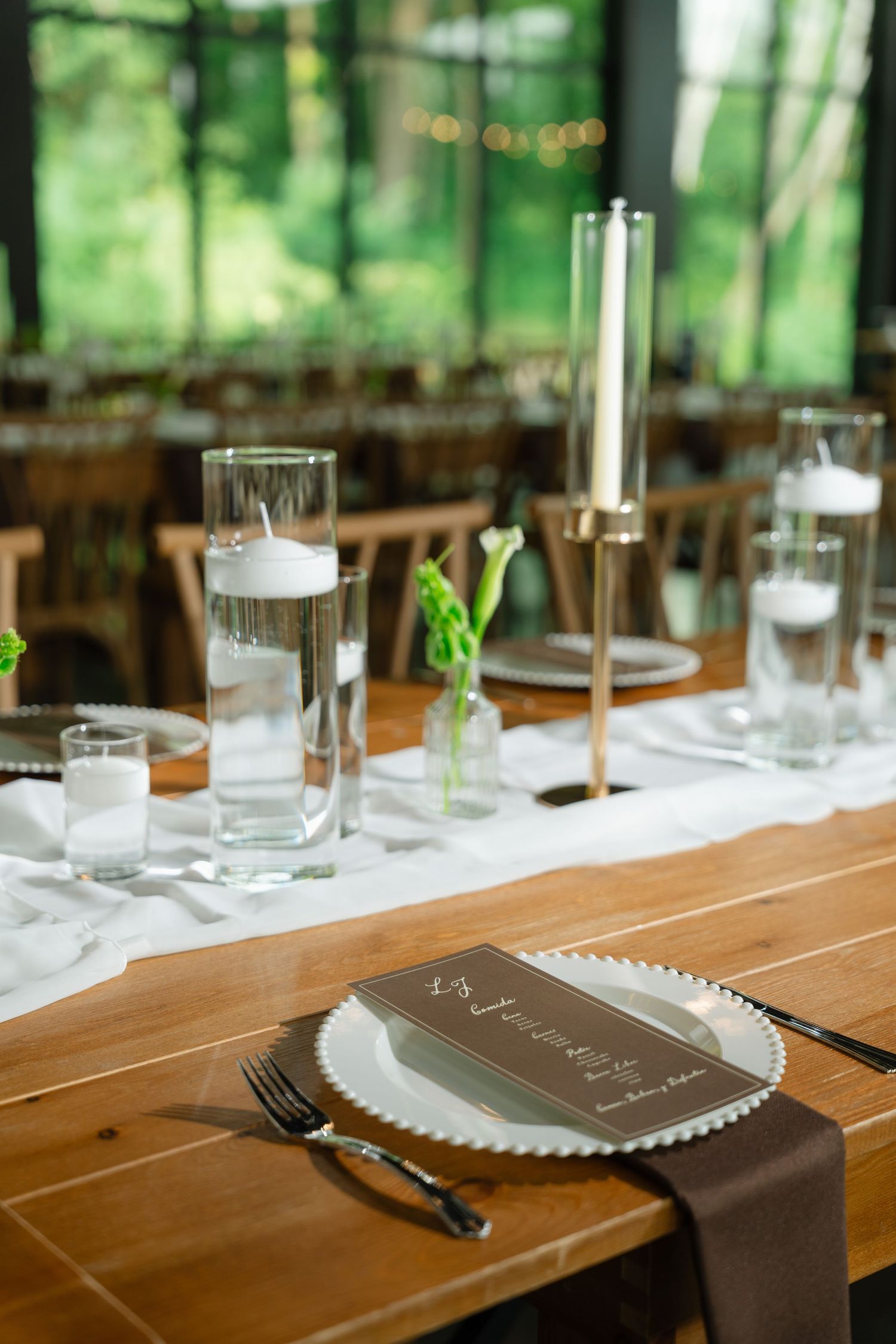 Wedding table centerpiece with floating candles, tall candleholders, and brown menu cards.