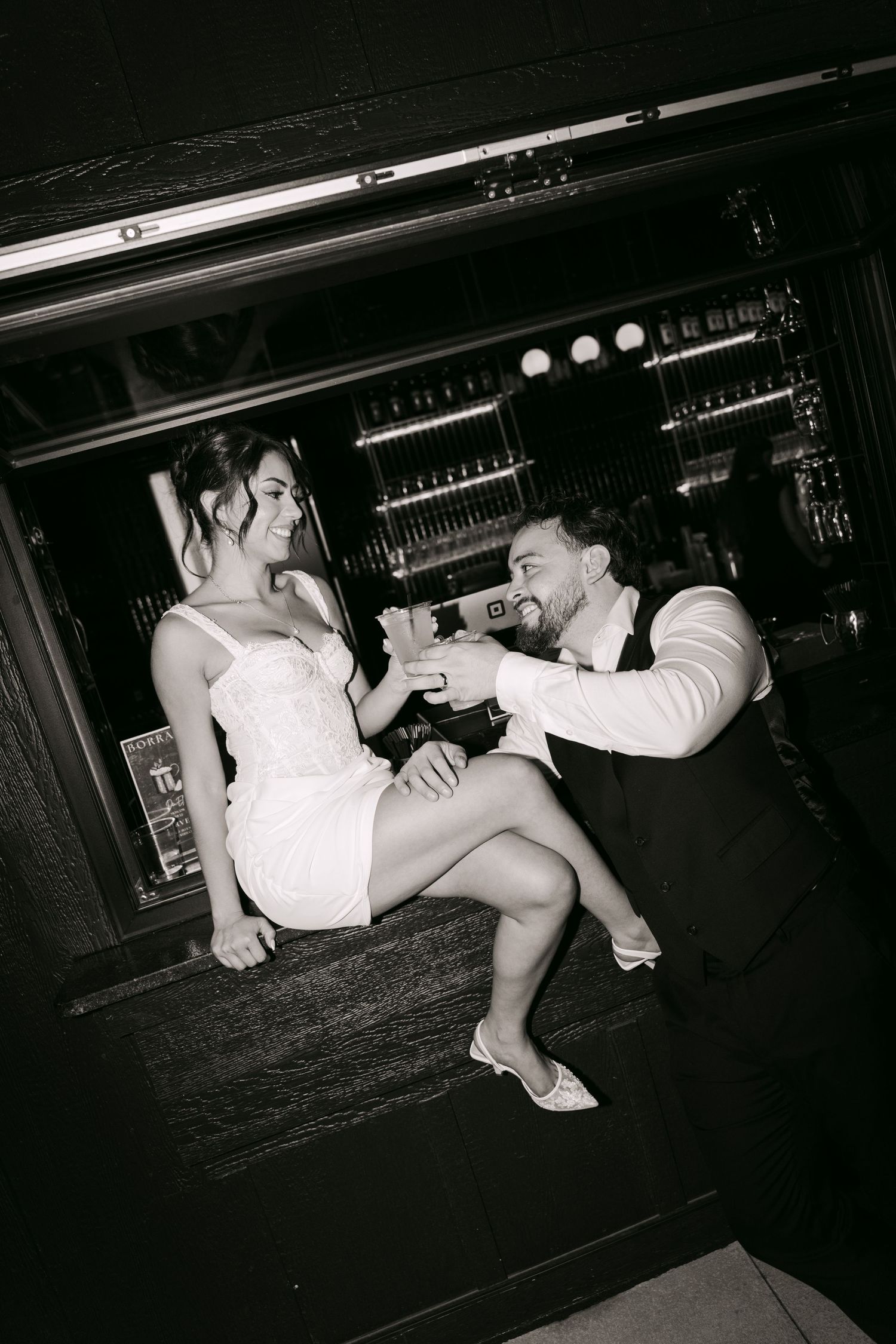 Bride and groom share a toast at a bar in elegant black and white wedding photo.