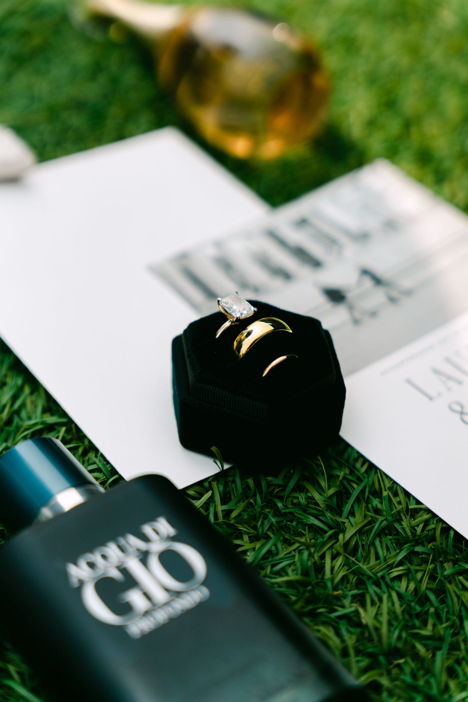 Close-up of gold wedding bands and diamond engagement ring in black velvet box with Acqua di Gio cologne.