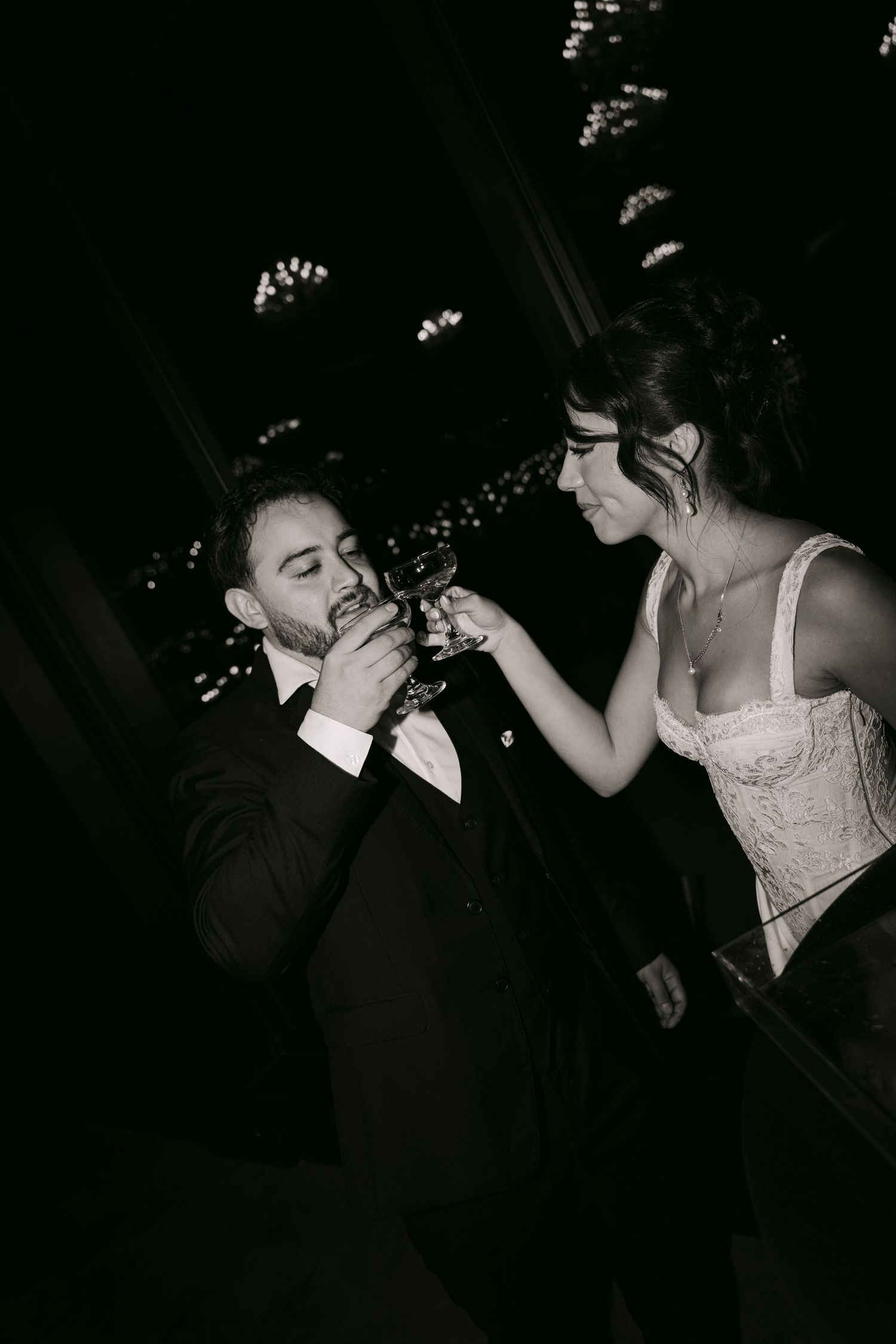 Black and white photo of bride and groom toasting champagne glasses at romantic wedding reception.