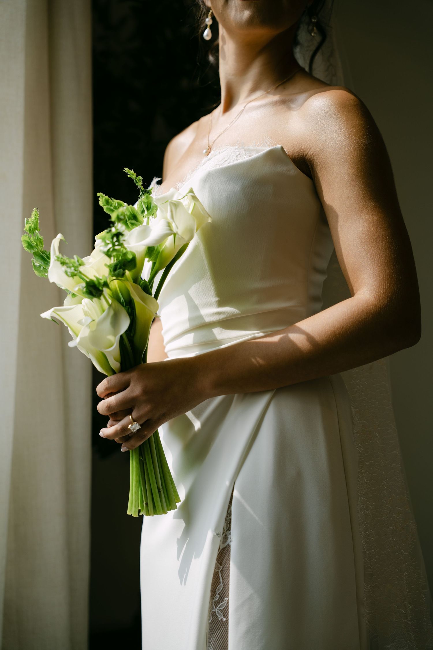 Bride in strapless white wedding gown holding an elegant white calla lily bridal bouquet.