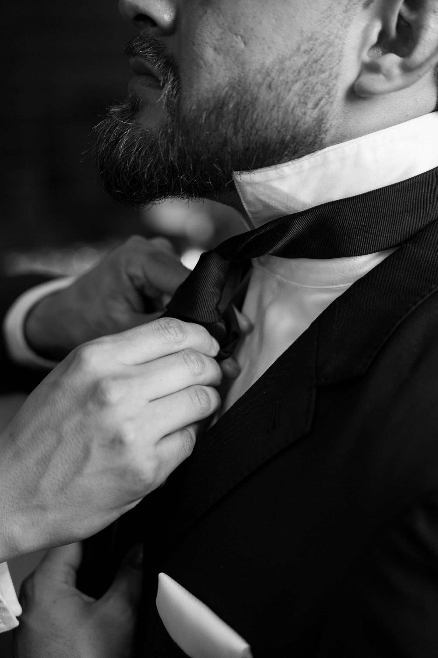 Close-up black and white photo of hands adjusting a grooms tie before the wedding ceremony.