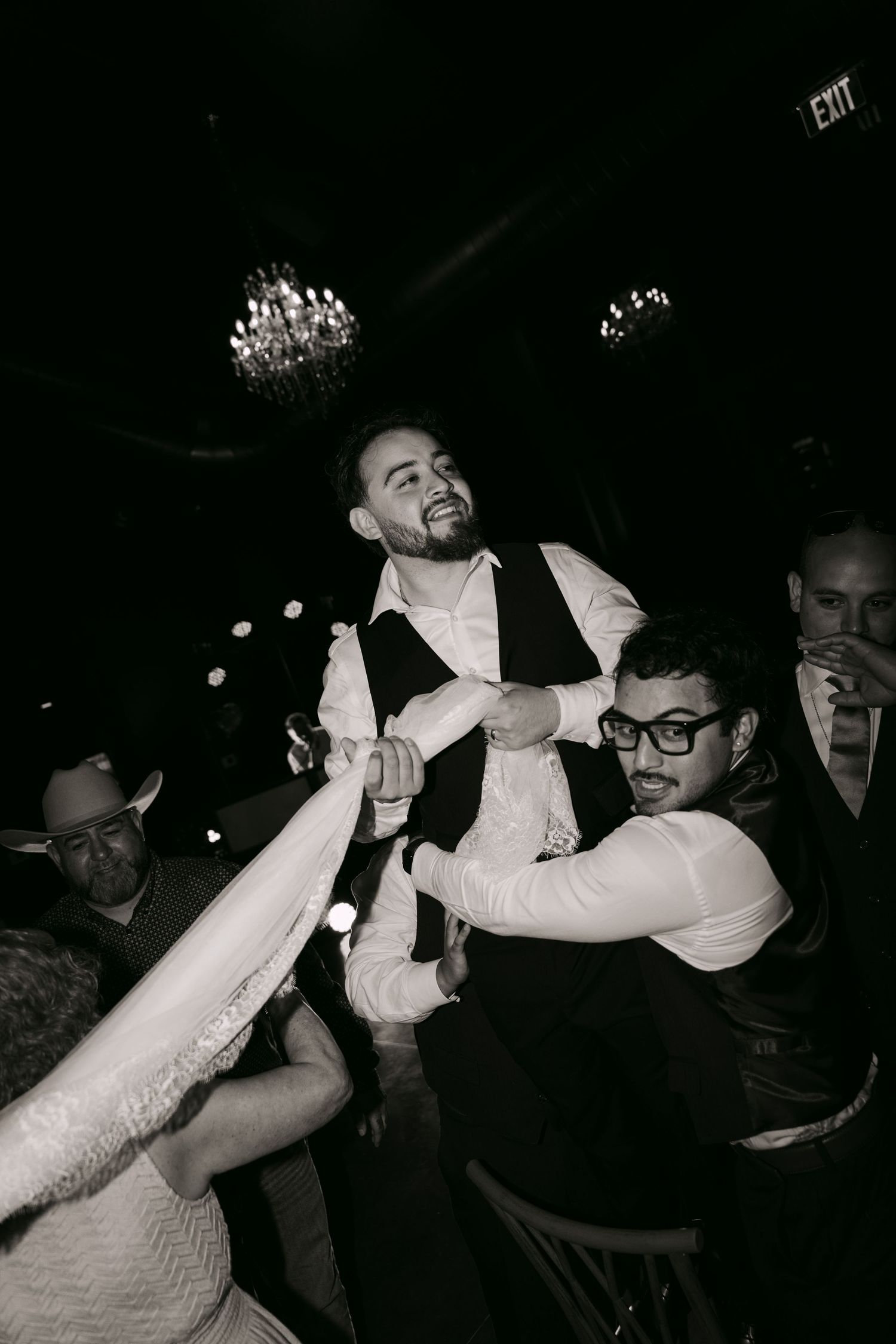 Groom lifted by groomsmen during lively black and white wedding reception celebration.