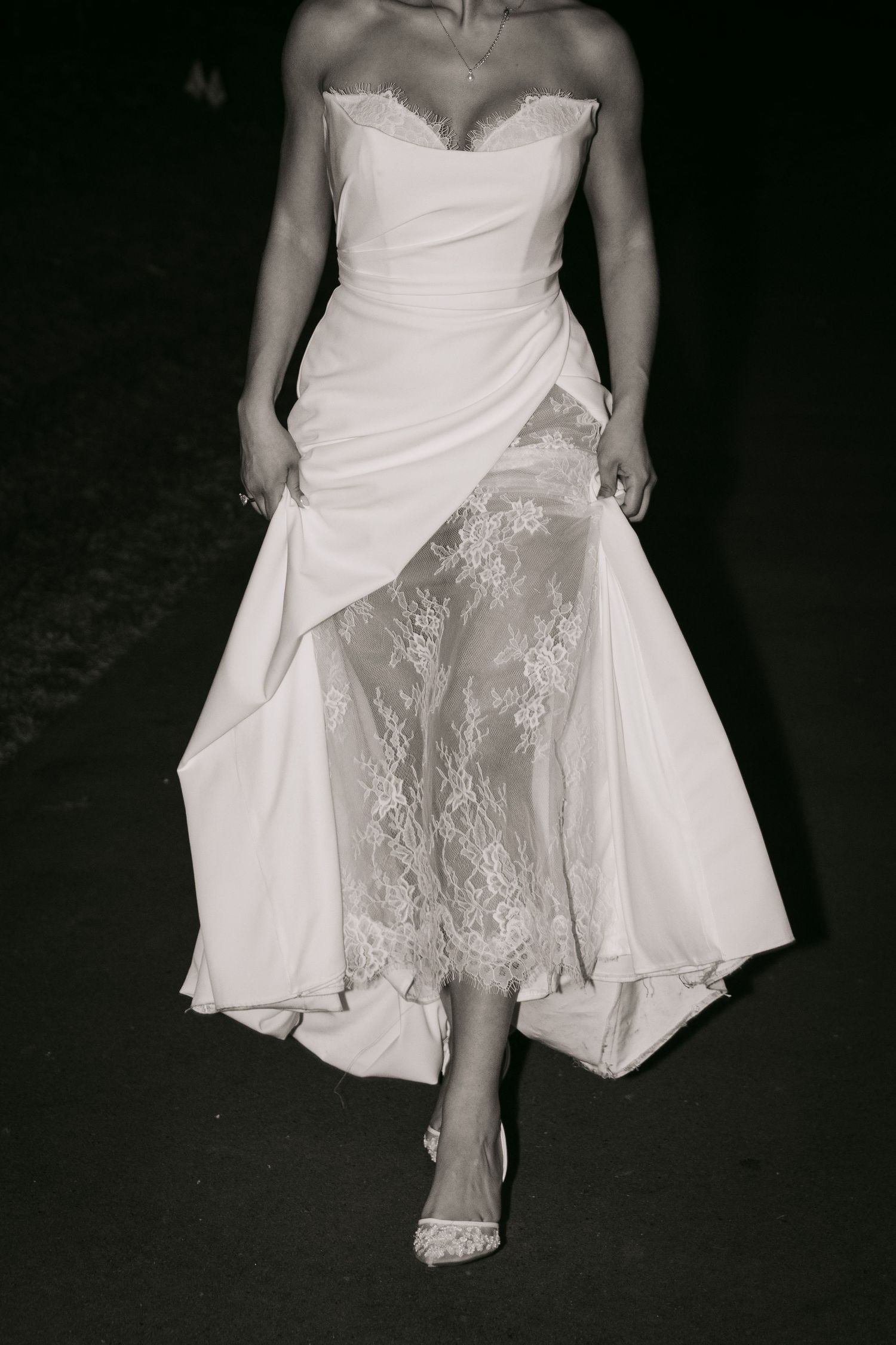 Black and white close-up of bride walking in strapless white gown with lace overlay detail.