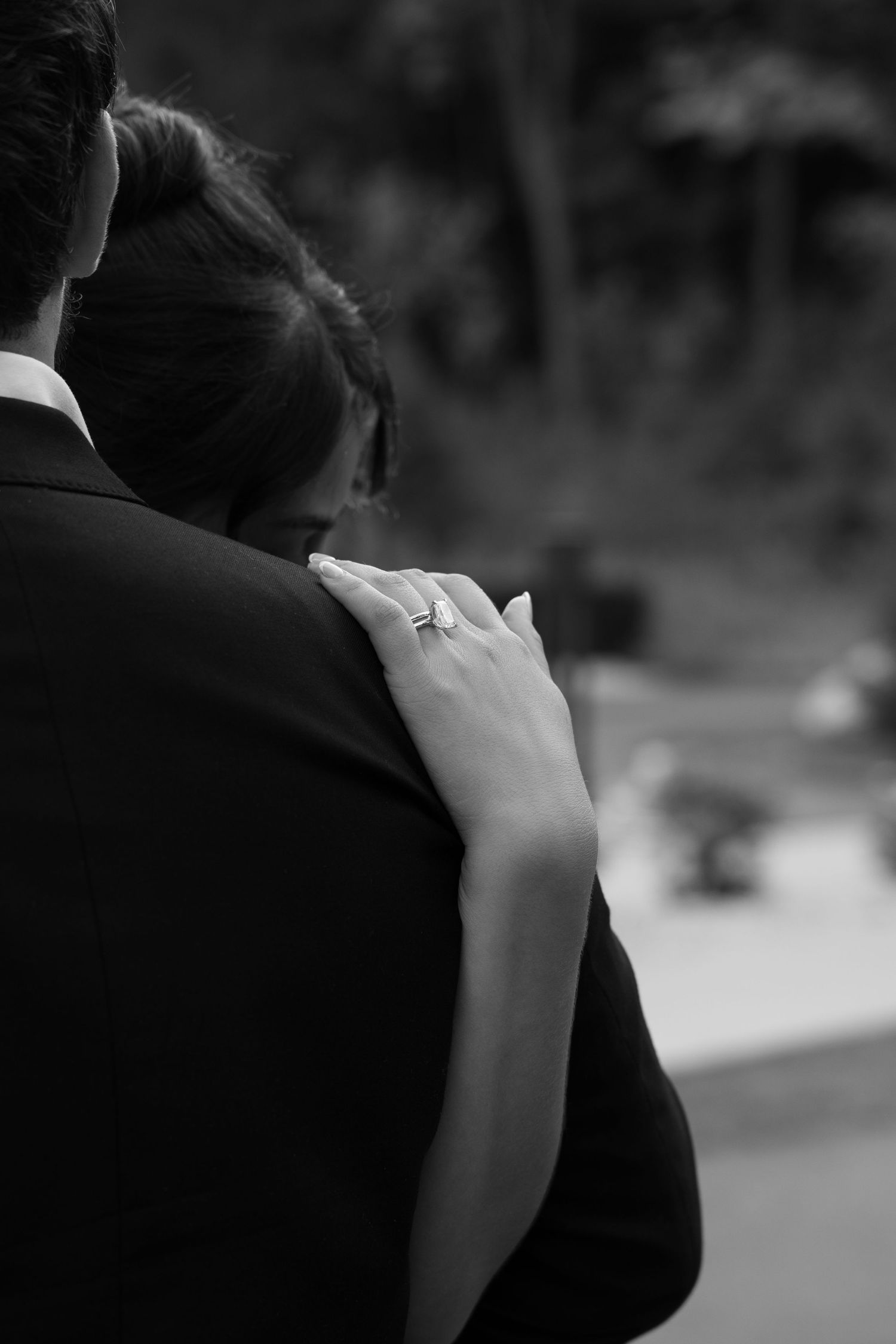 Close-up black and white photo of bride resting hand with engagement ring on grooms shoulder.