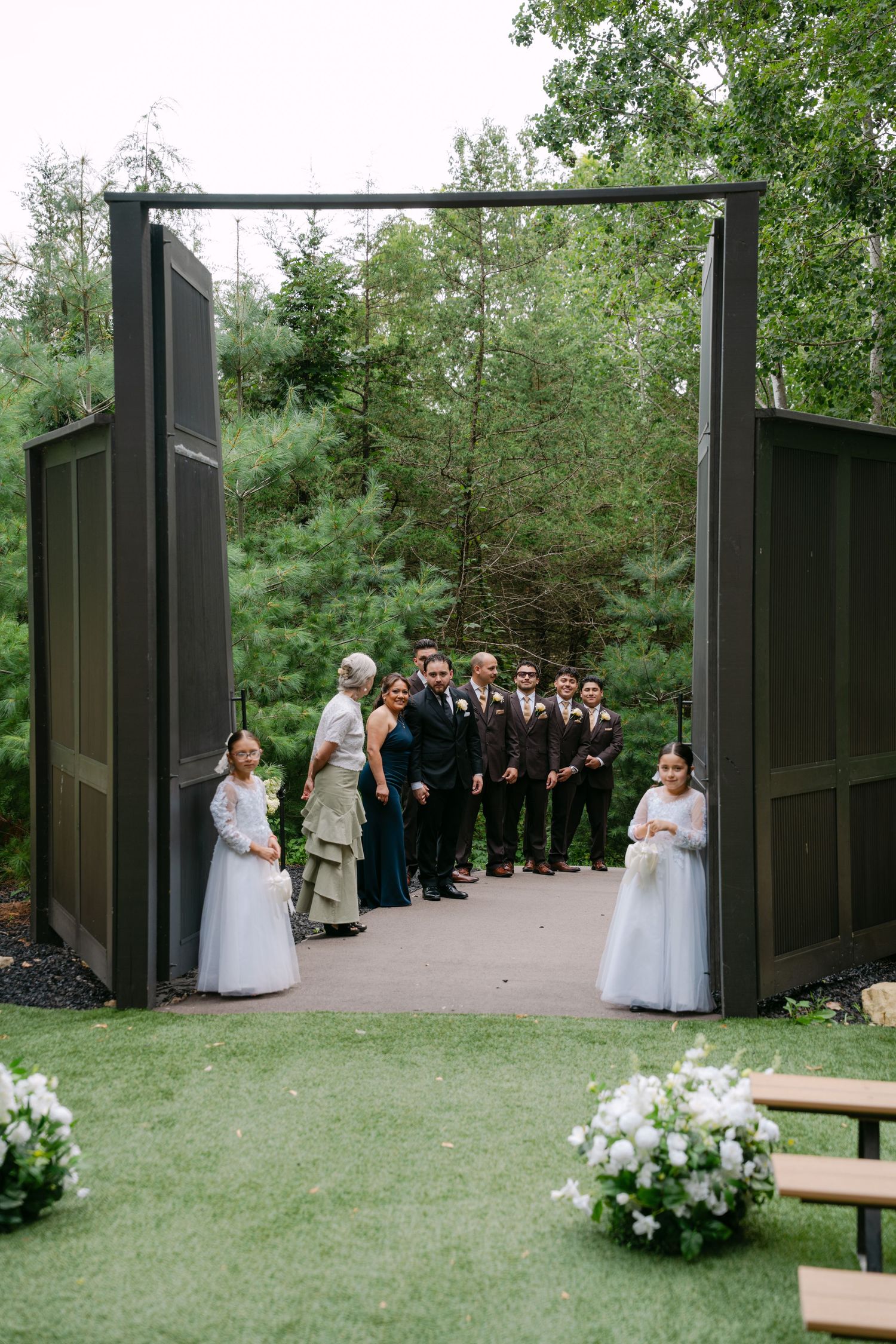 Wedding party standing in doorway of large dark wooden gates at outdoor garden ceremony entrance.