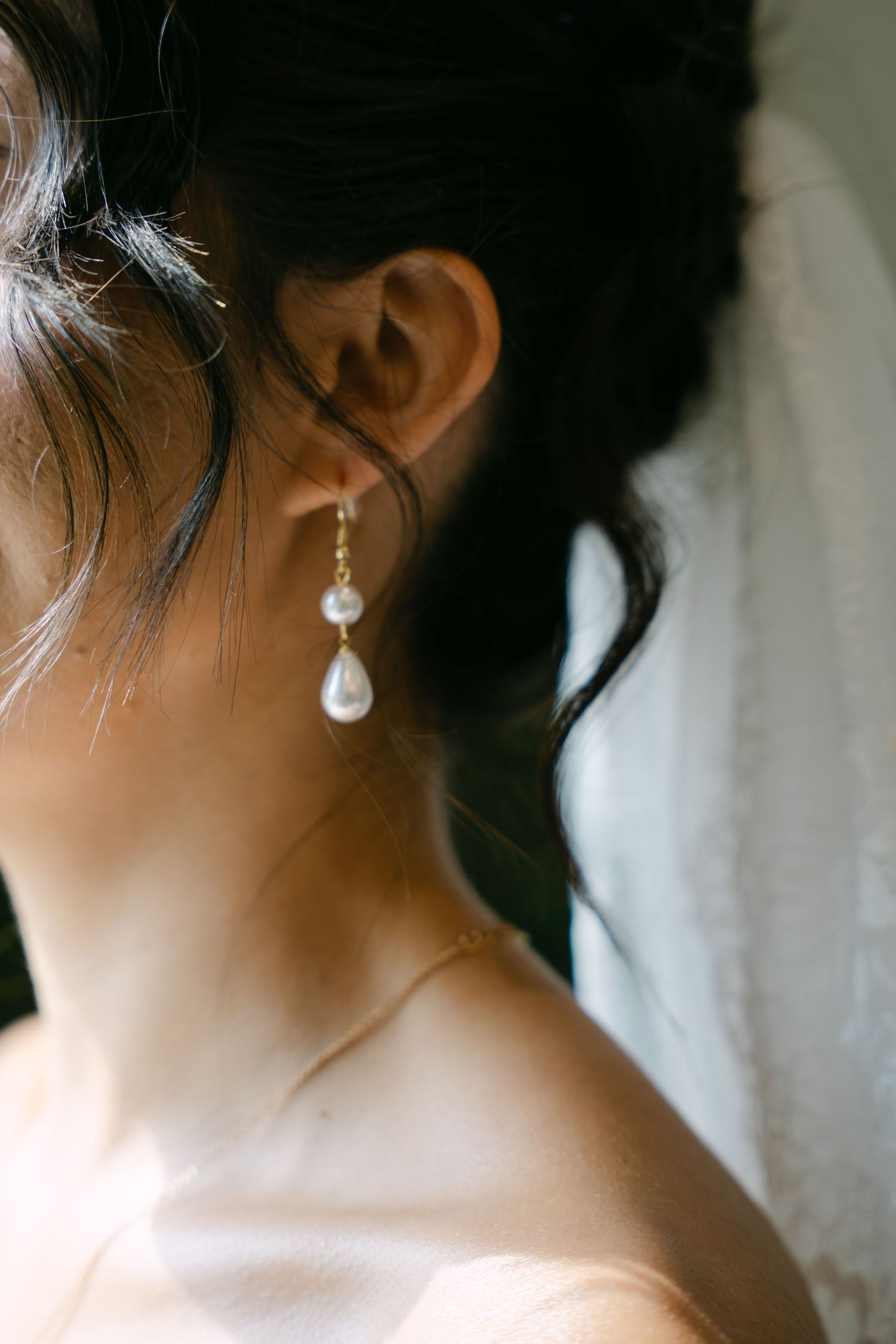 Close-up detail of brides pearl drop earring with upswept dark hair on wedding day.