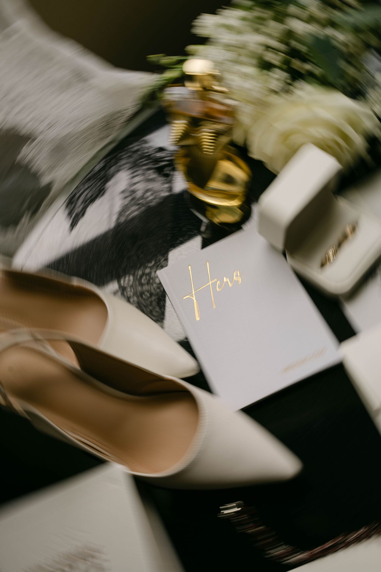 Elegant wedding flat lay with cream heels, gold accents, white flowers, and a personalized Hera card on dark background.