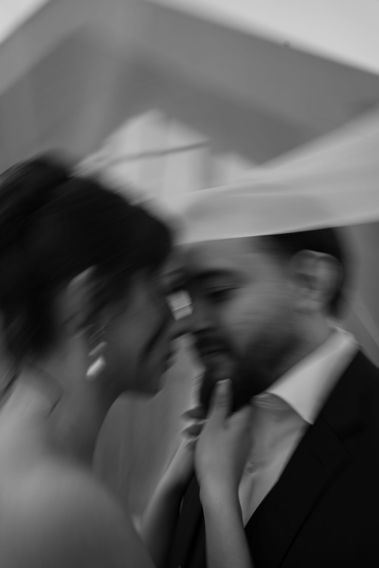 Artistic blurred black and white photo of bride and groom sharing an intimate moment under veil.