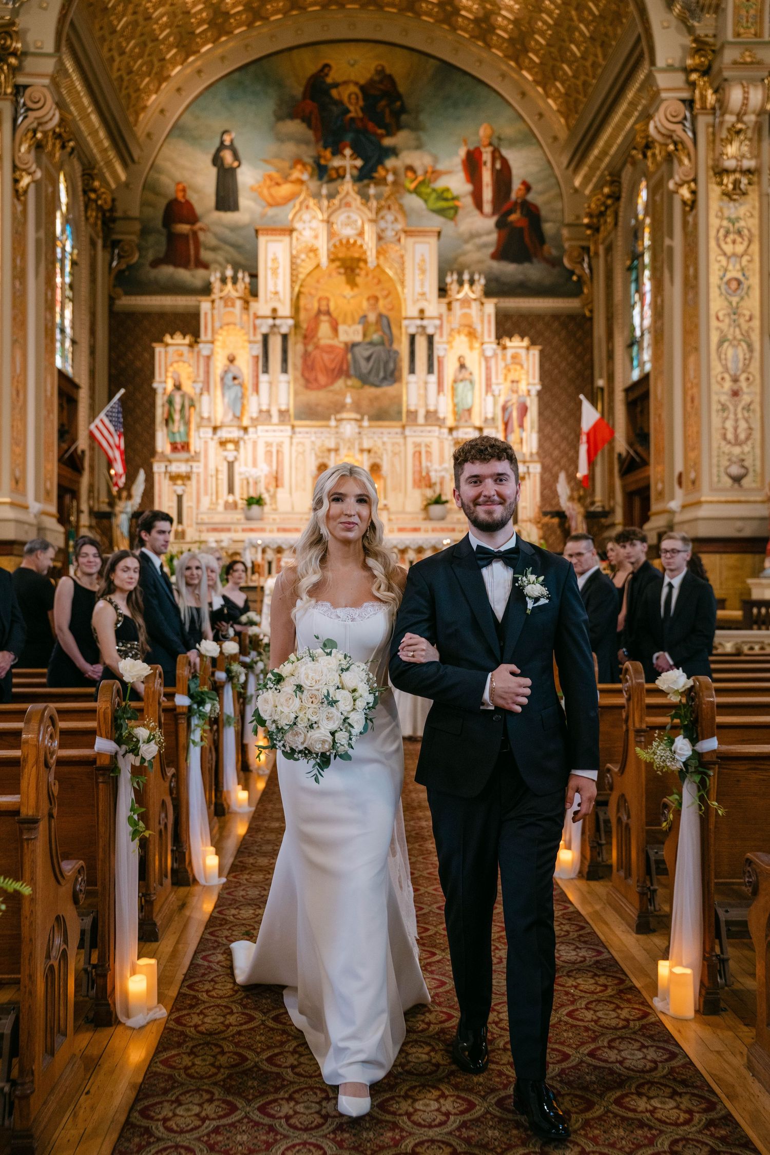 Bride and groom walk down the aisle of a stunning ornate church after their wedding ceremony.