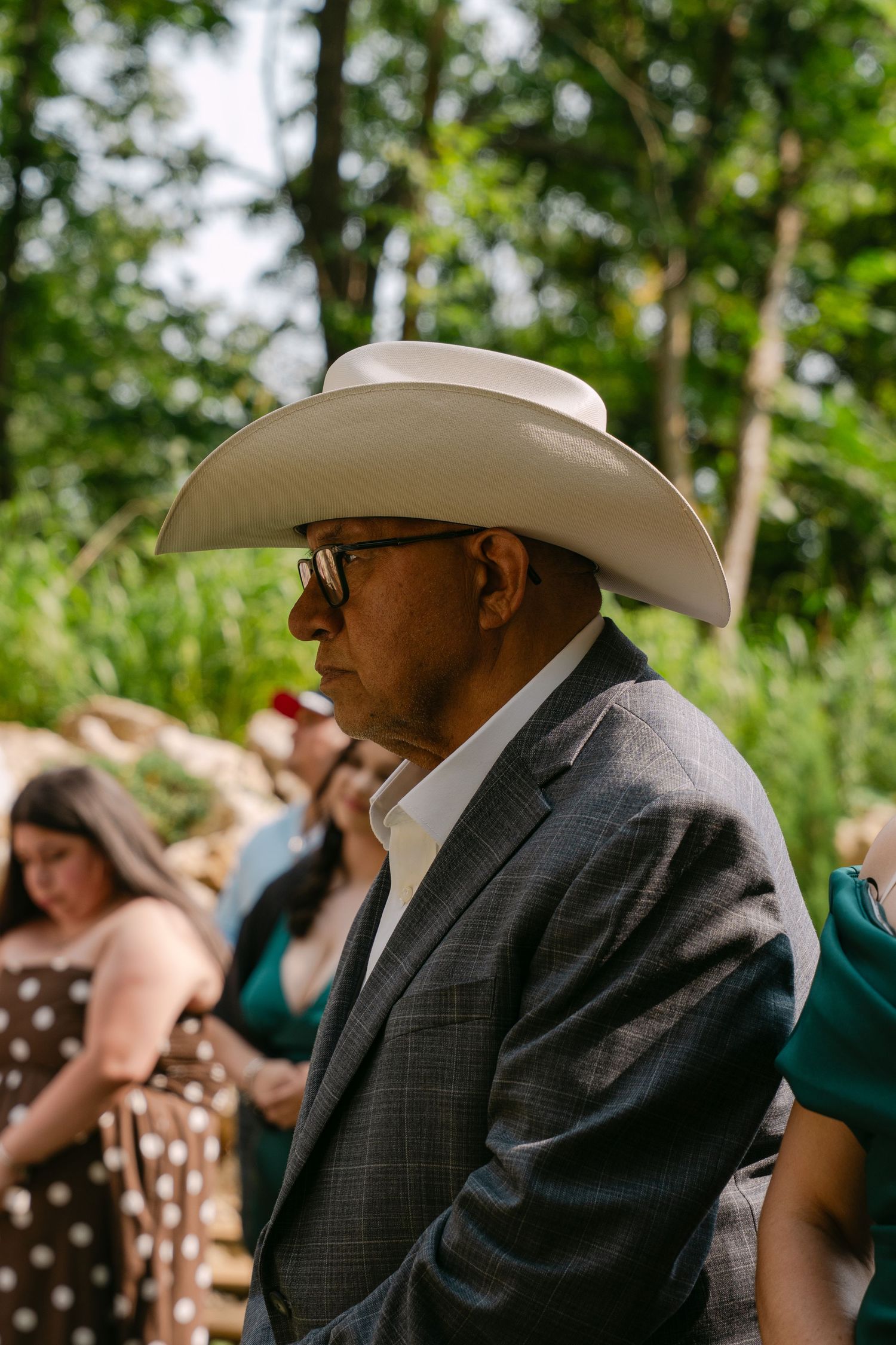 Distinguished older man in gray suit and white cowboy hat attends outdoor wedding ceremony.
