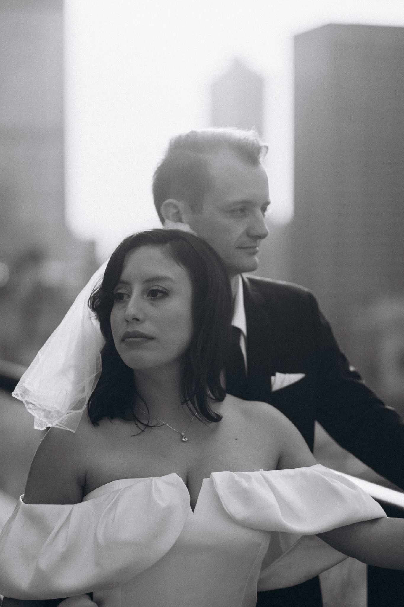 Black and white portrait of bride in white veil and groom in dark suit in urban setting.