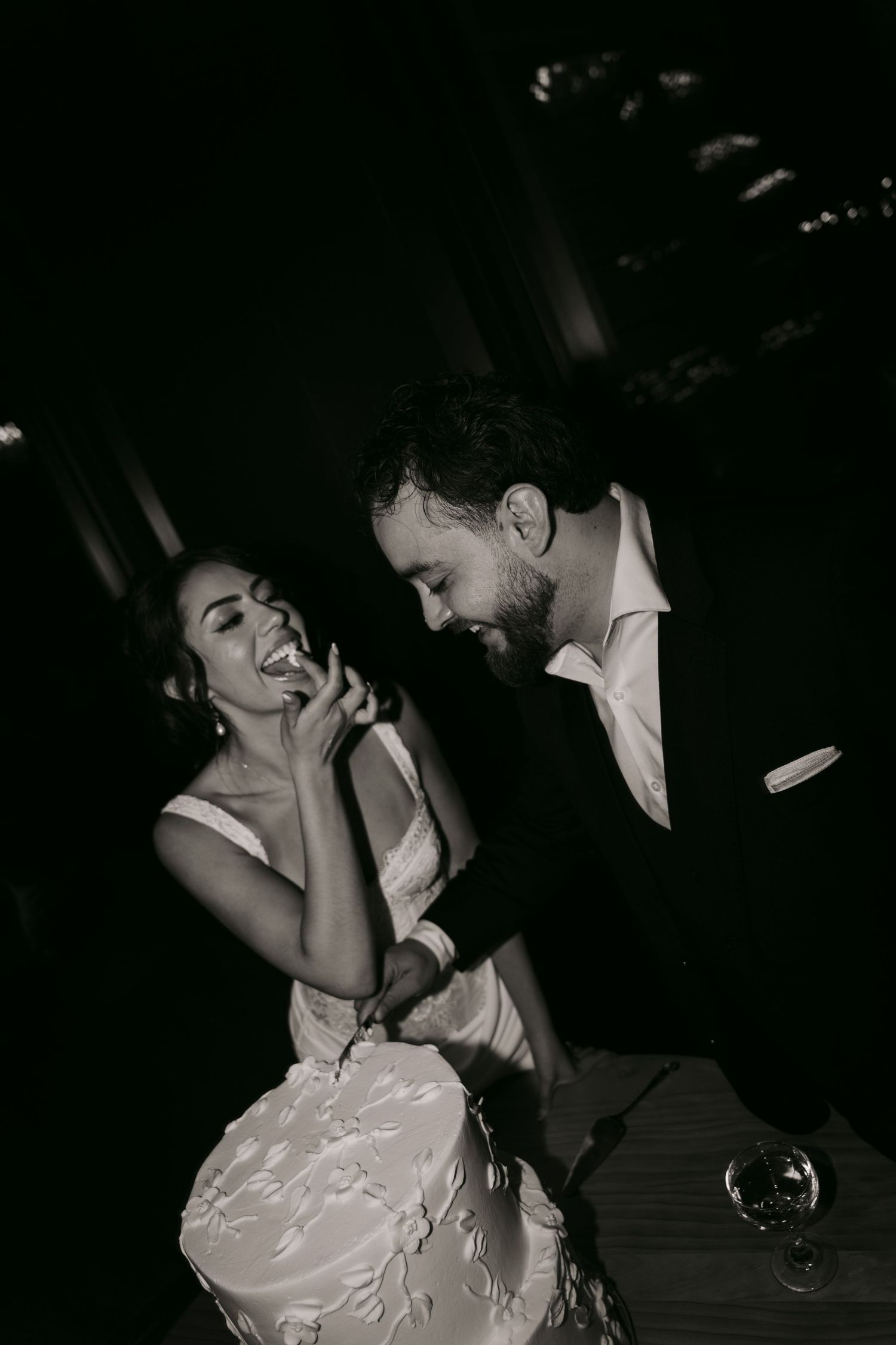 Black and white photo of joyful bride and groom laughing together at romantic wedding reception.