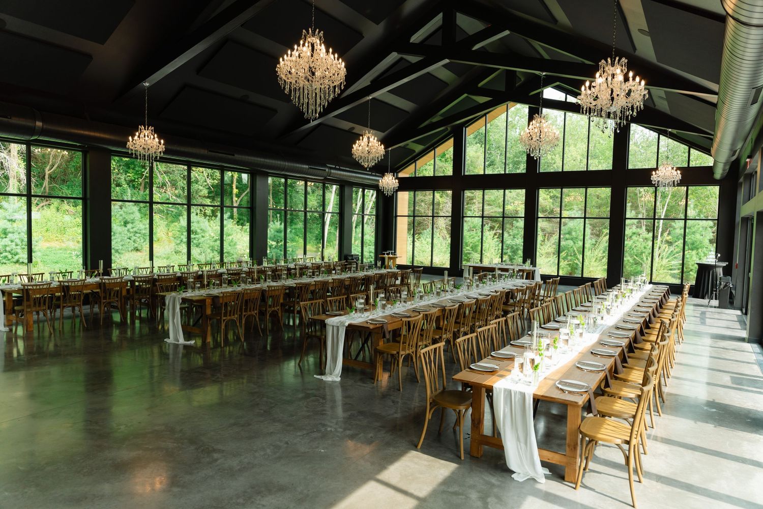 Spacious wedding venue with multiple long tables, crystal chandeliers, and garden views.