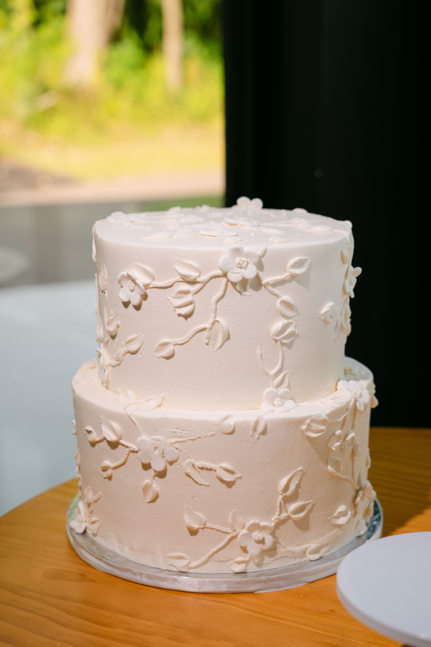 Two-tier white wedding cake decorated with delicate fondant floral and vine designs on wood table.