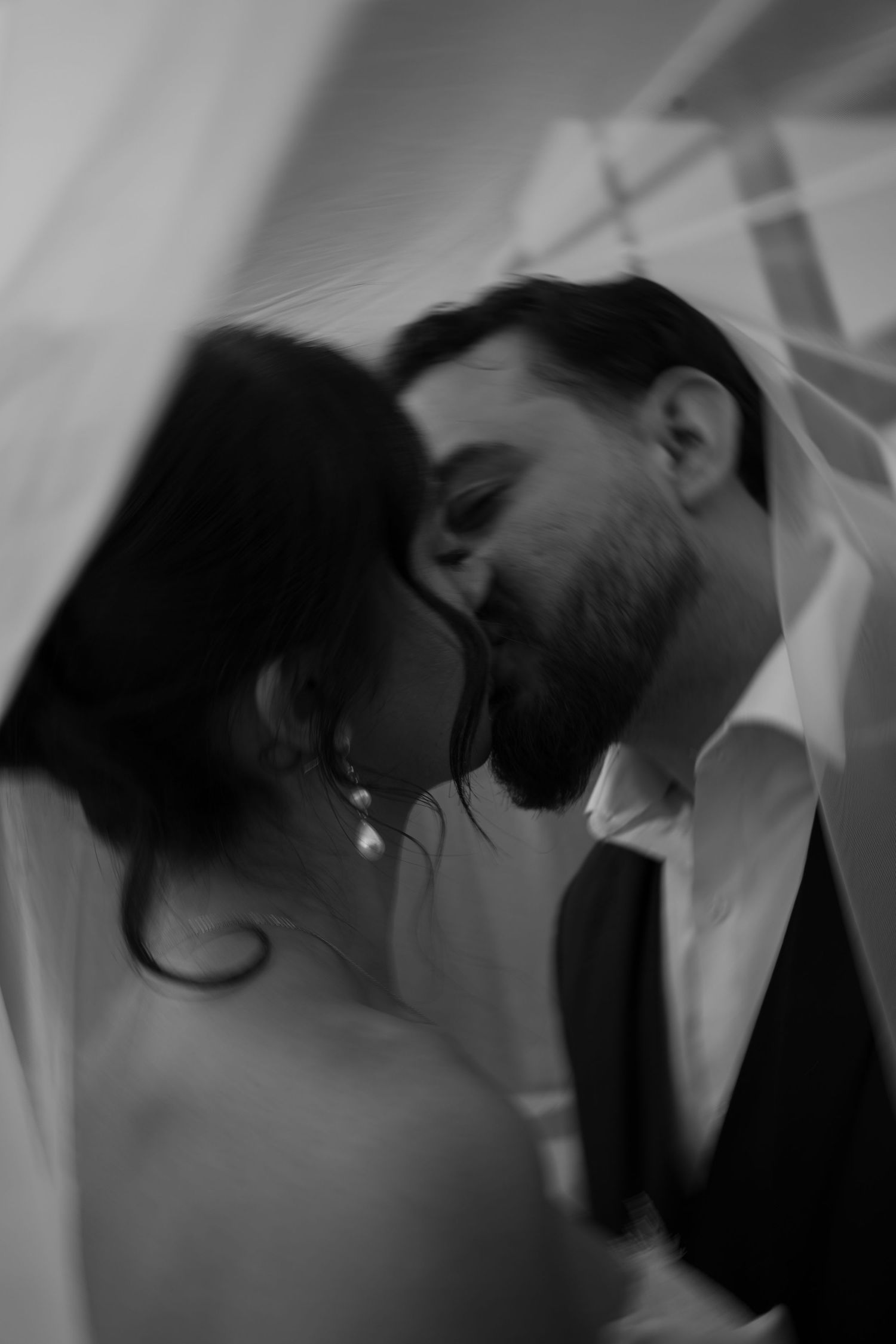 Romantic black and white photo of bride and groom kissing beneath a flowing wedding veil.
