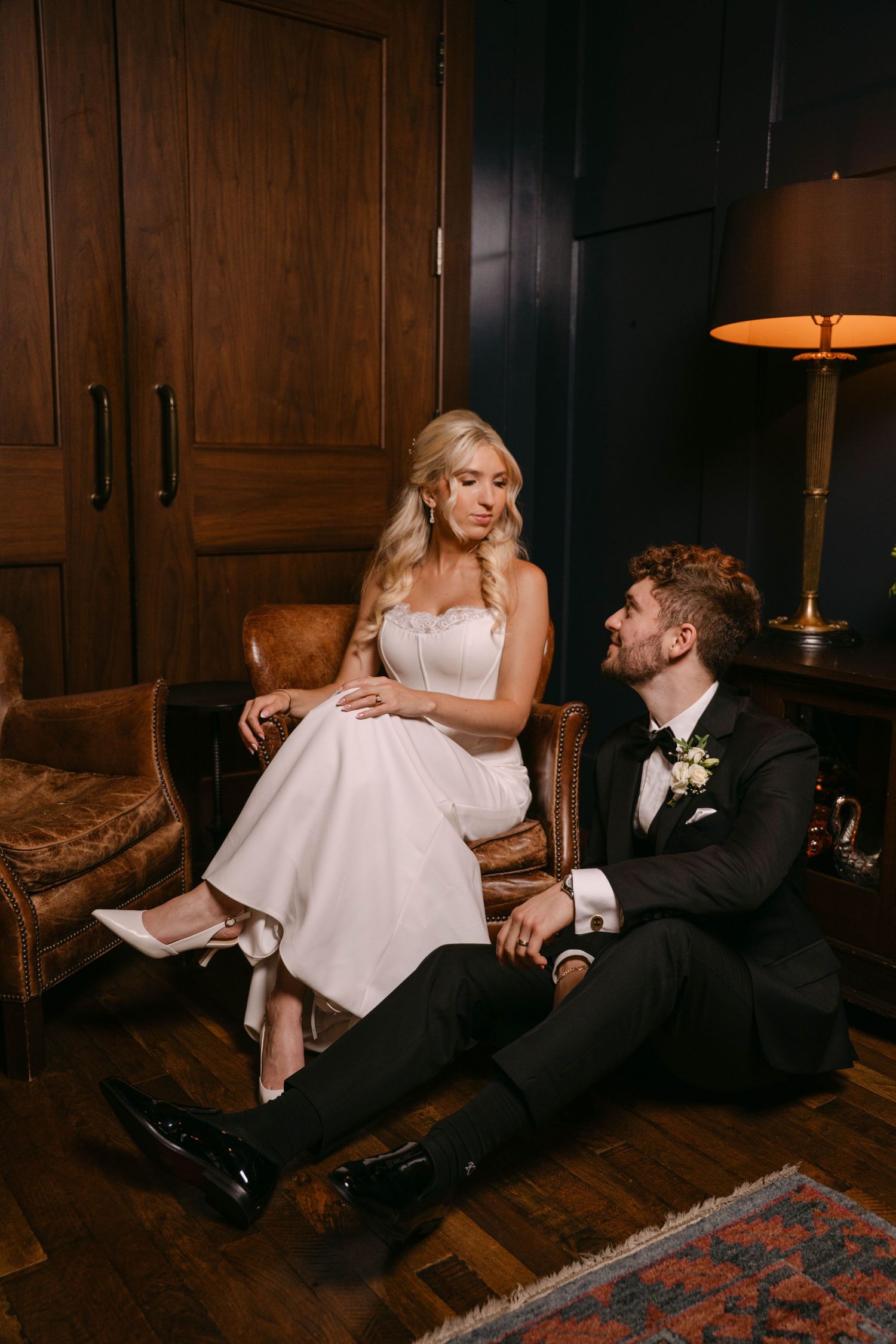 Bride in strapless white dress and groom in tuxedo sharing a romantic moment in a stylish room.